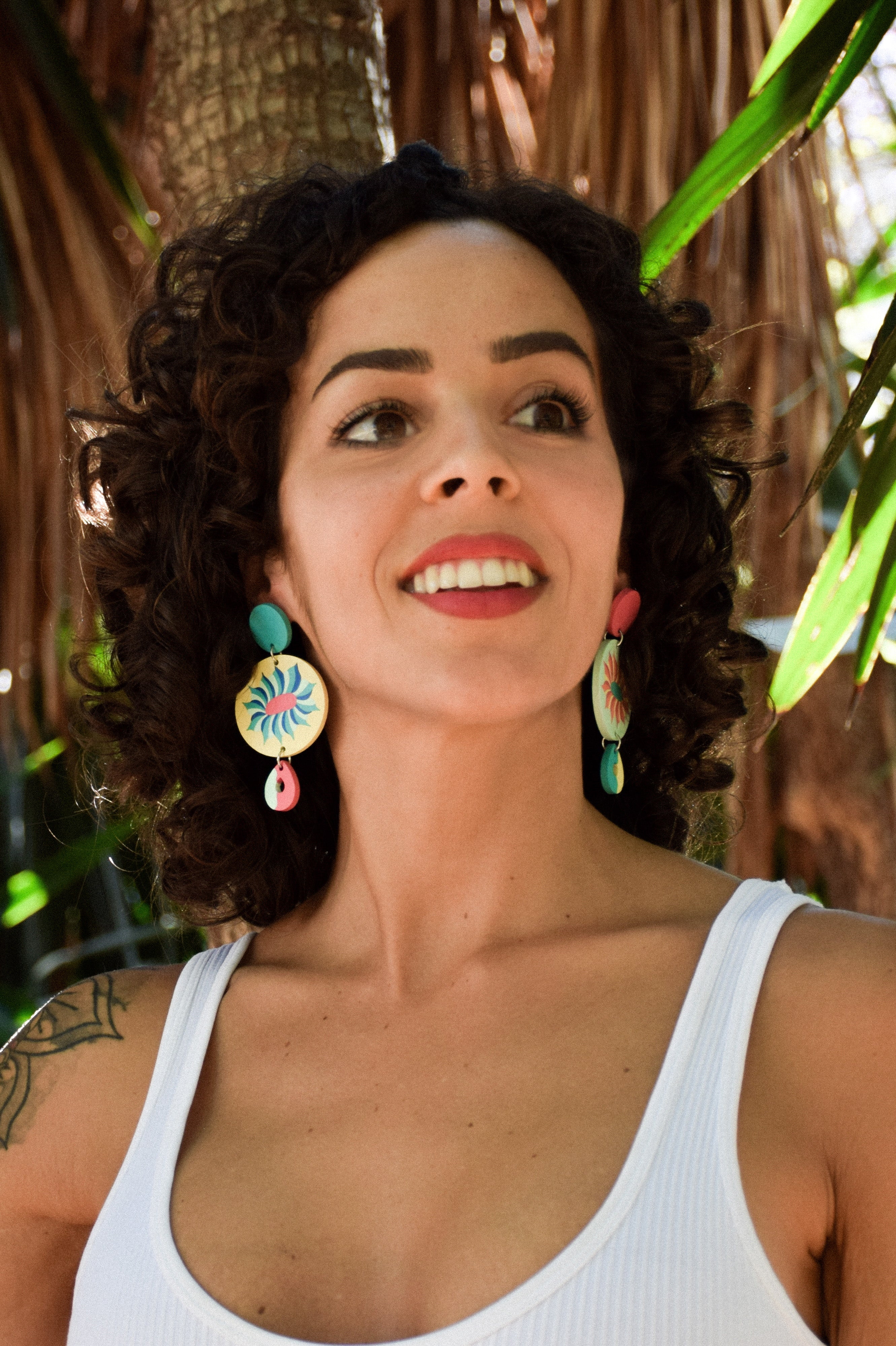 Woman with curly hair and colorful earrings standing outdoors with trees in the background