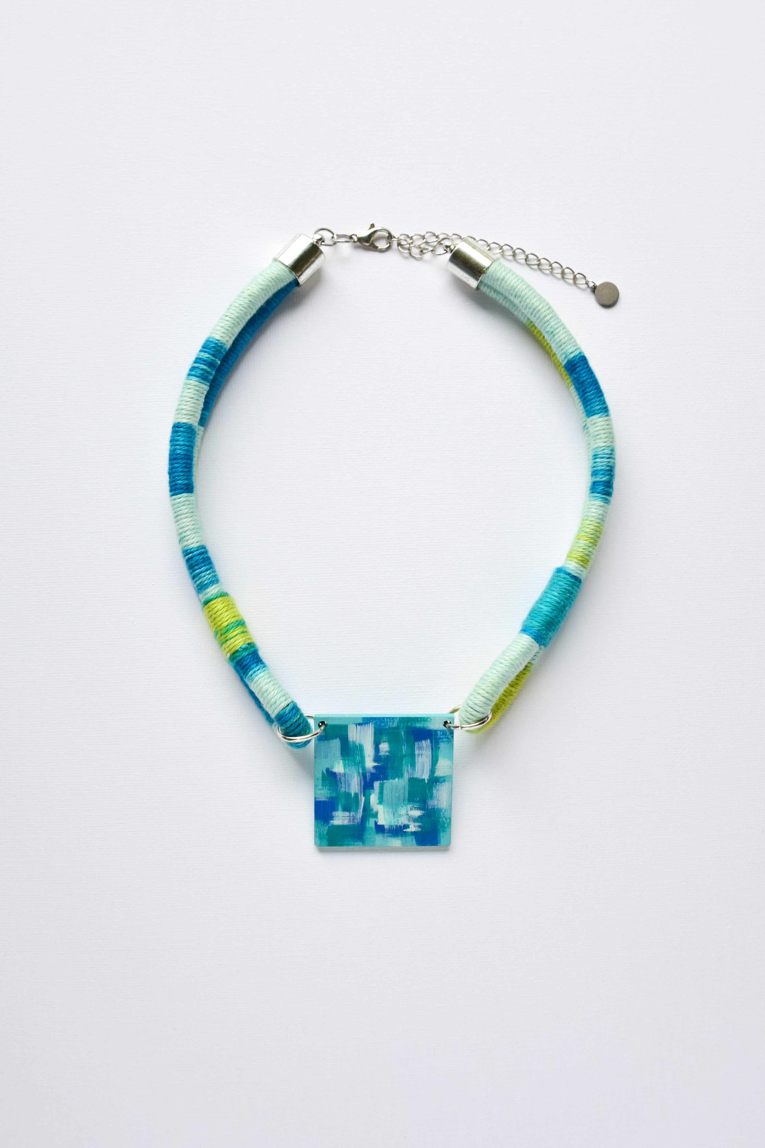 Necklace with blue and green wrapped cord and square pendant on a white background