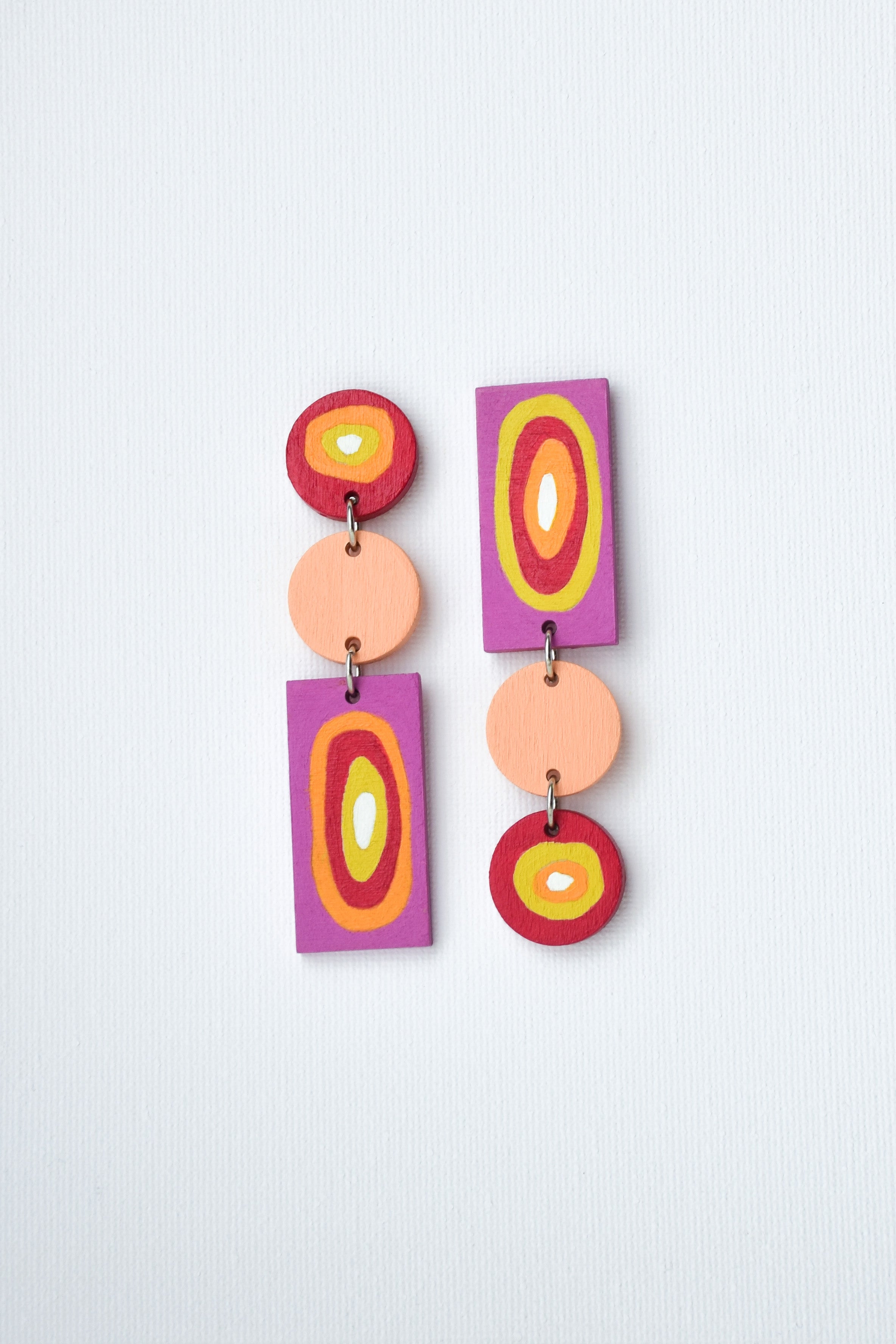 Colorful hand-painted earrings with circular and rectangular shapes on a light gray background