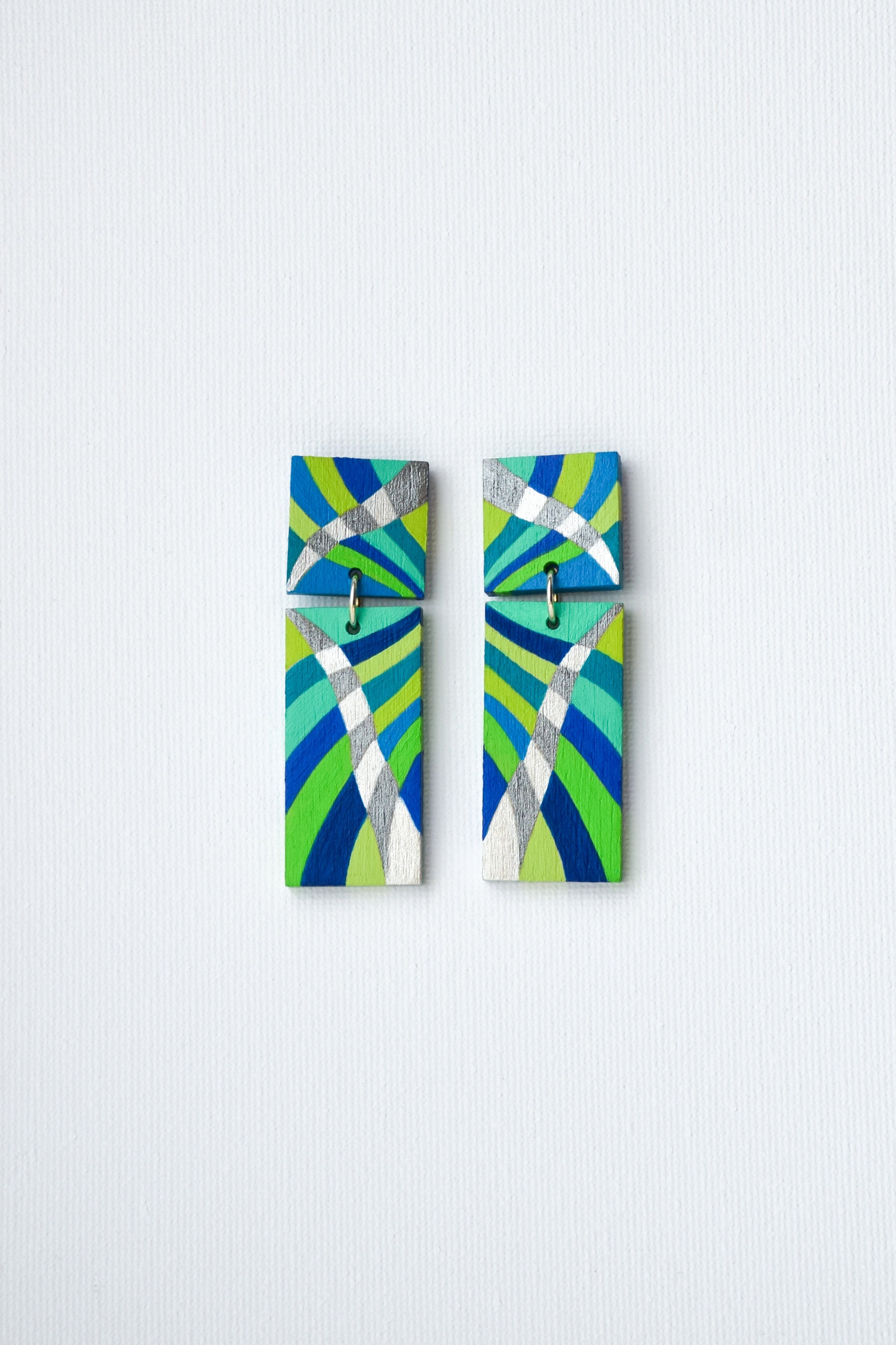 Pair of hand-painted earrings with green and blue abstract design on a light gray background