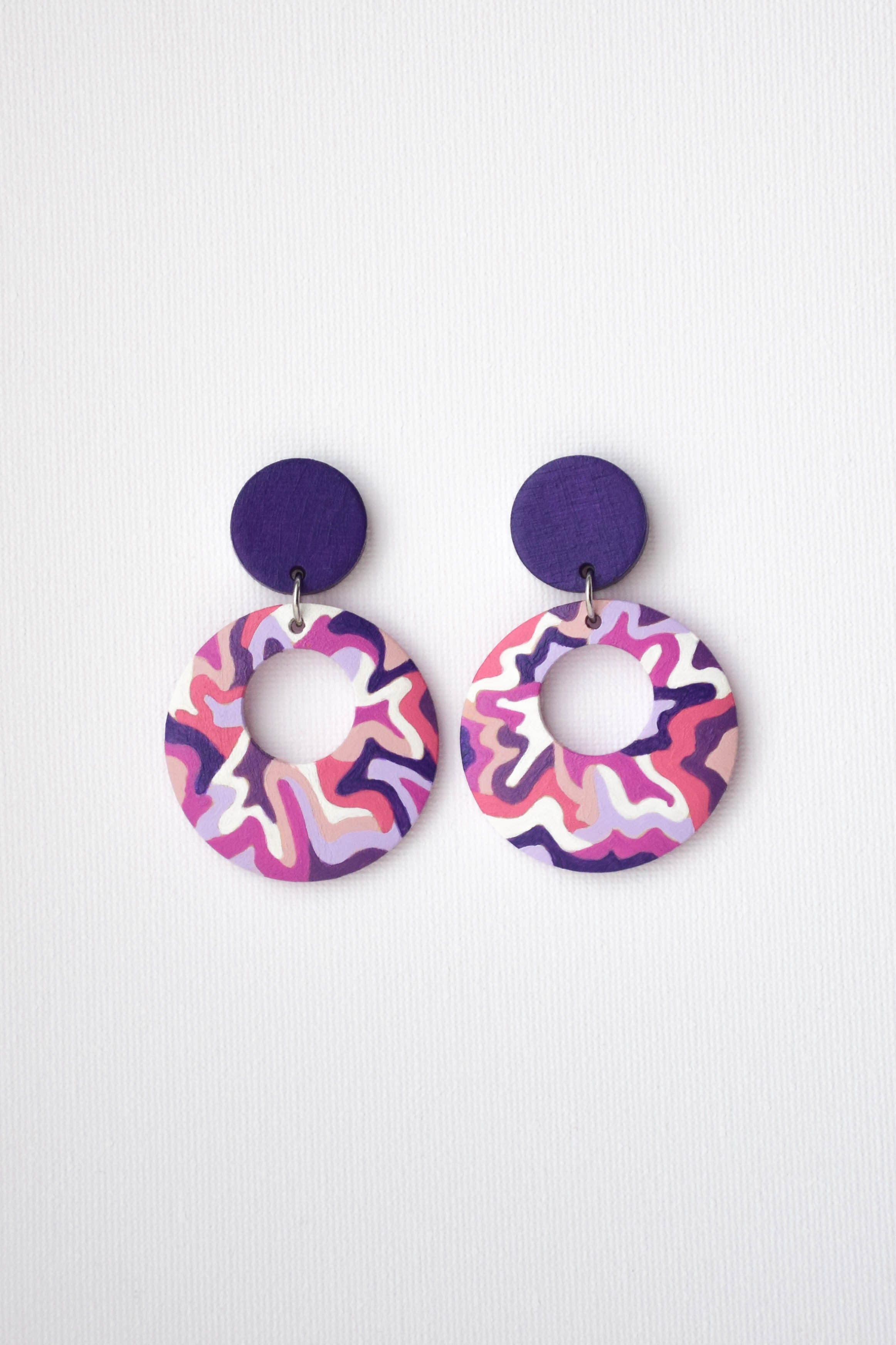 Pair of colorful earrings with purple posts on a white background