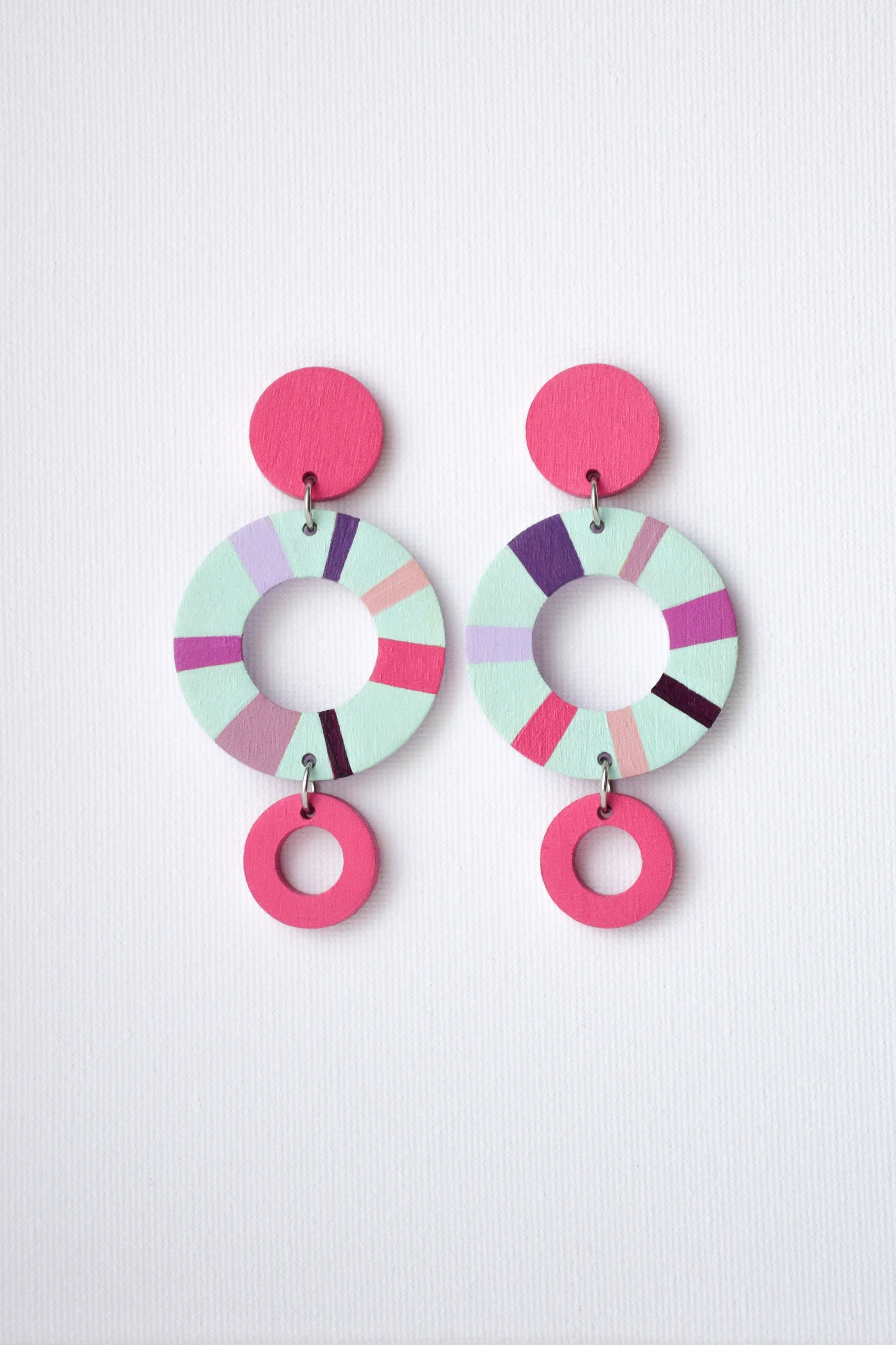 Colorful hand-painted circular earrings in pastel colors on a light gray background
