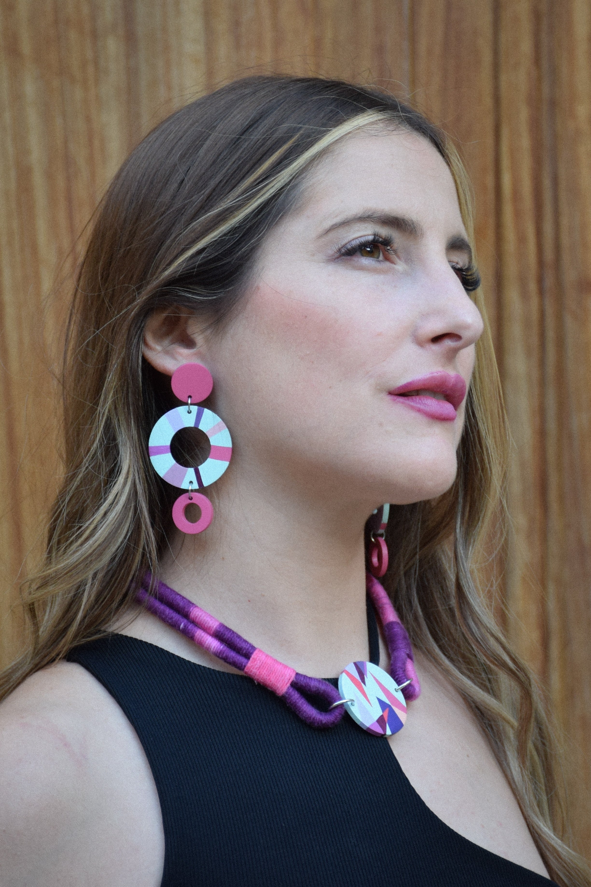 Woman wearing colorful earrings and necklace against a wooden background