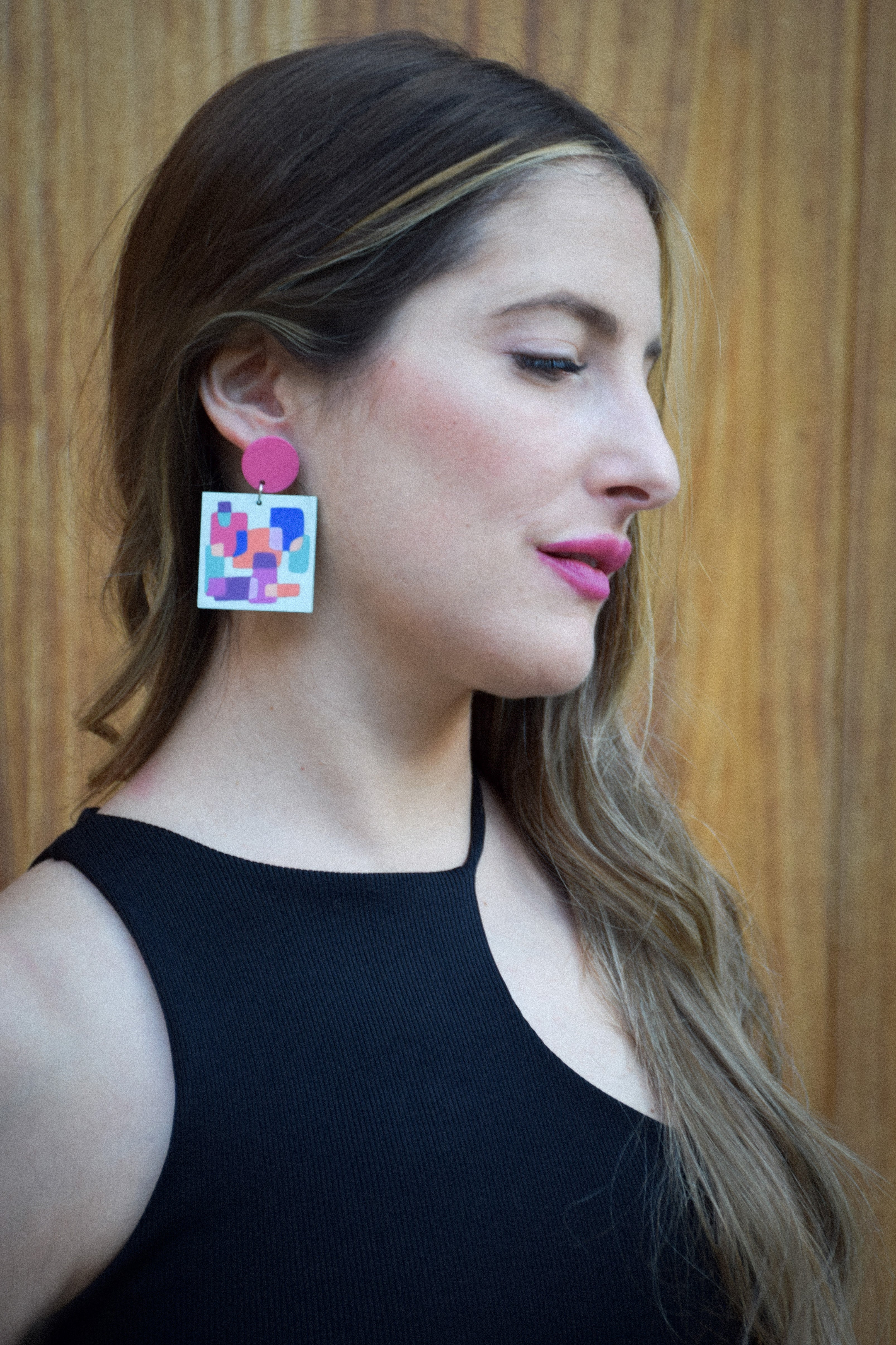 Woman wearing colorful geometric earrings against a wooden background