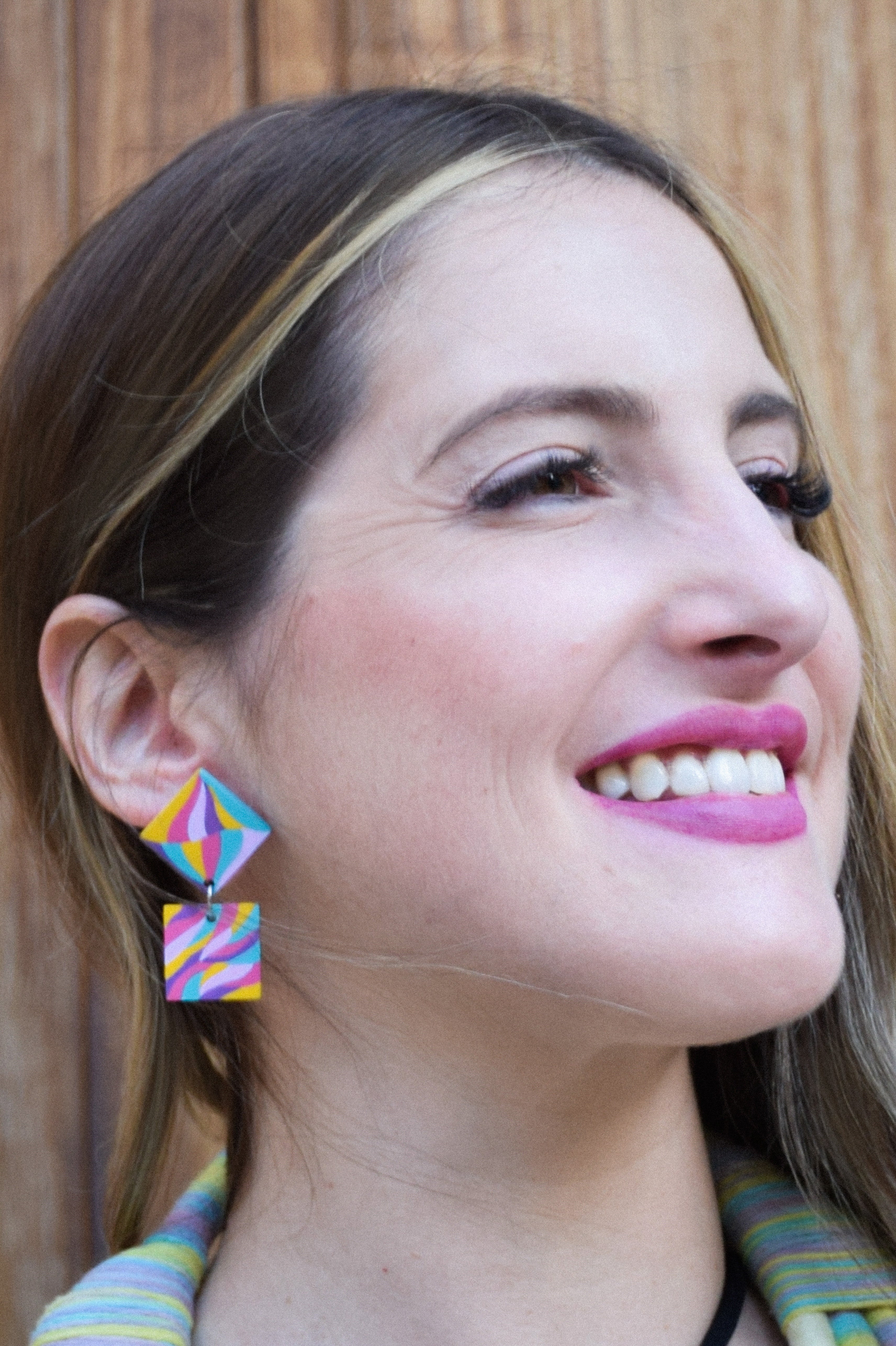 Woman wearing colorful hand-painted geometric earrings with a wooden background