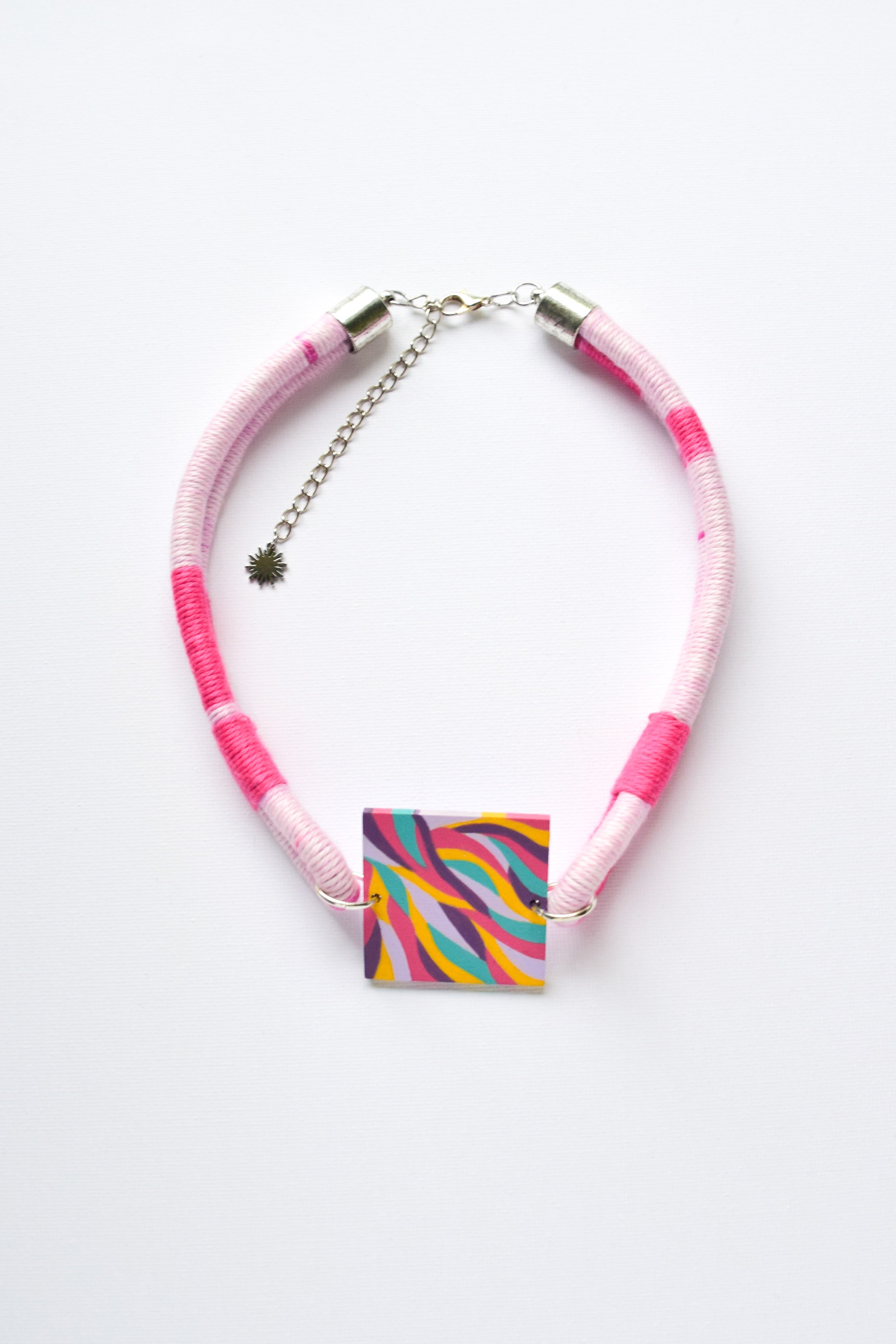 Necklace with pink and white wrapped cord and colorful square pendant on a white background