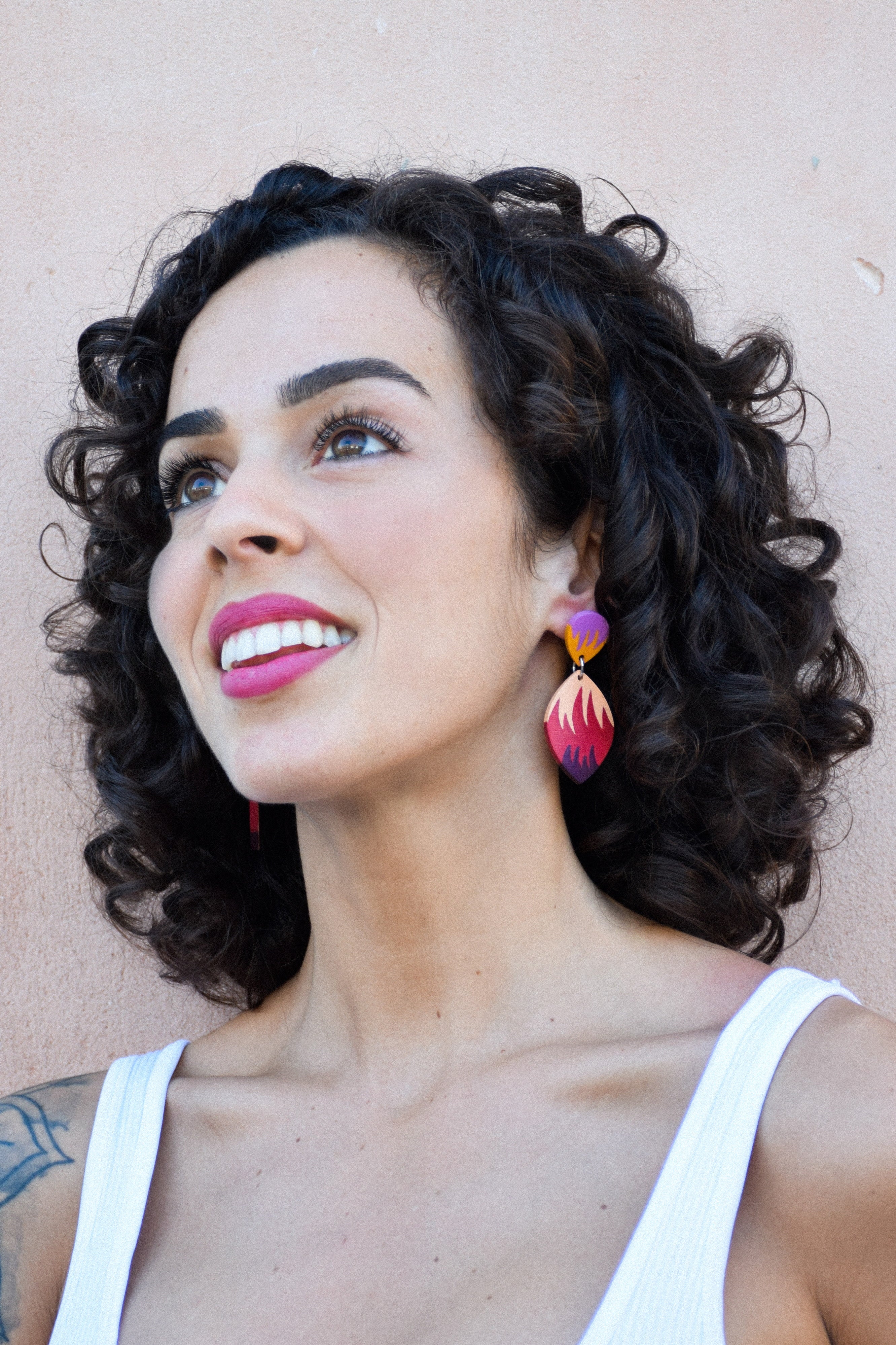 Woman with curly hair wearing colorful earrings against a beige background