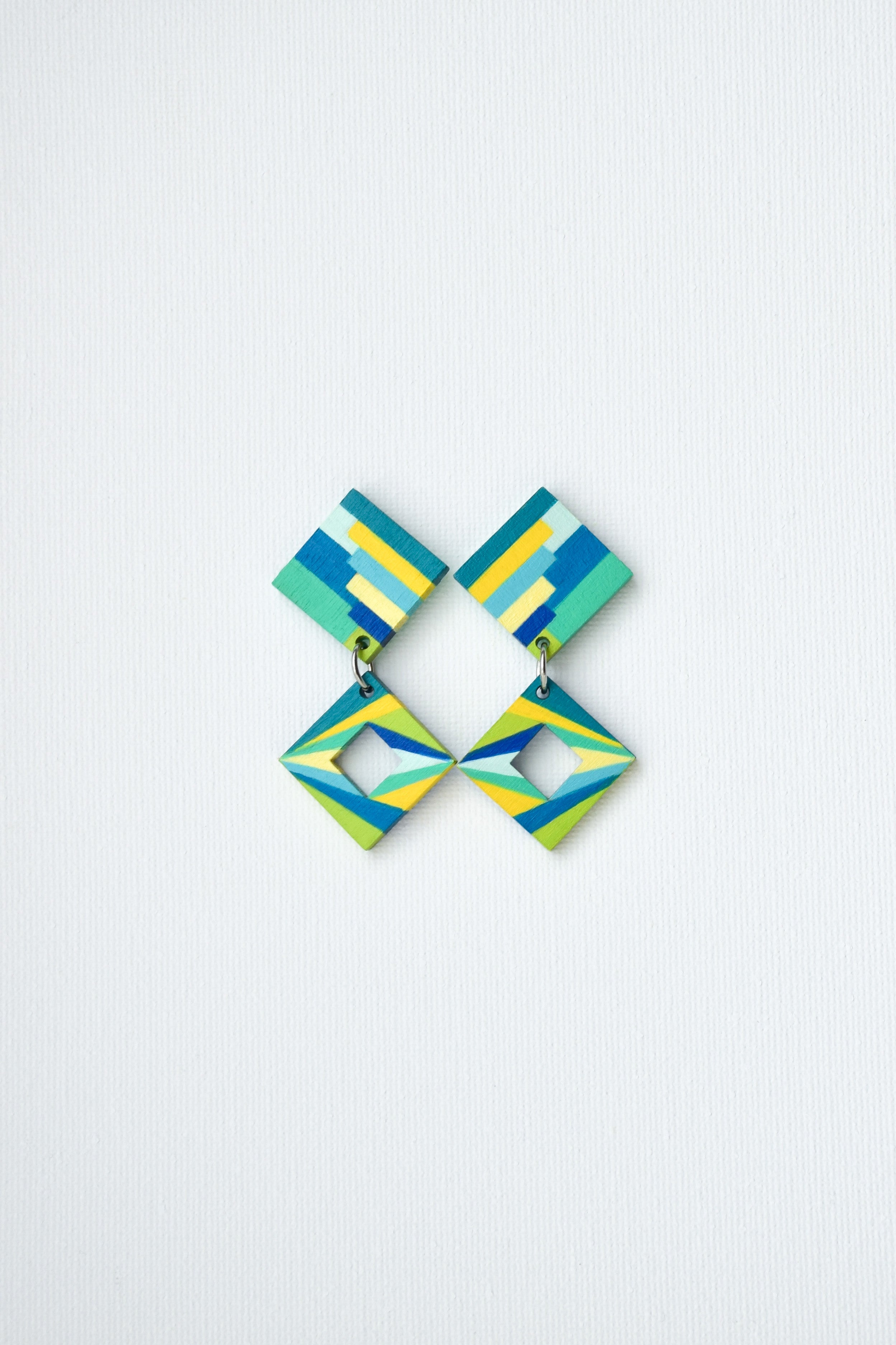 Pair of hand-painted geometric earrings with blue and green design on a light gray background