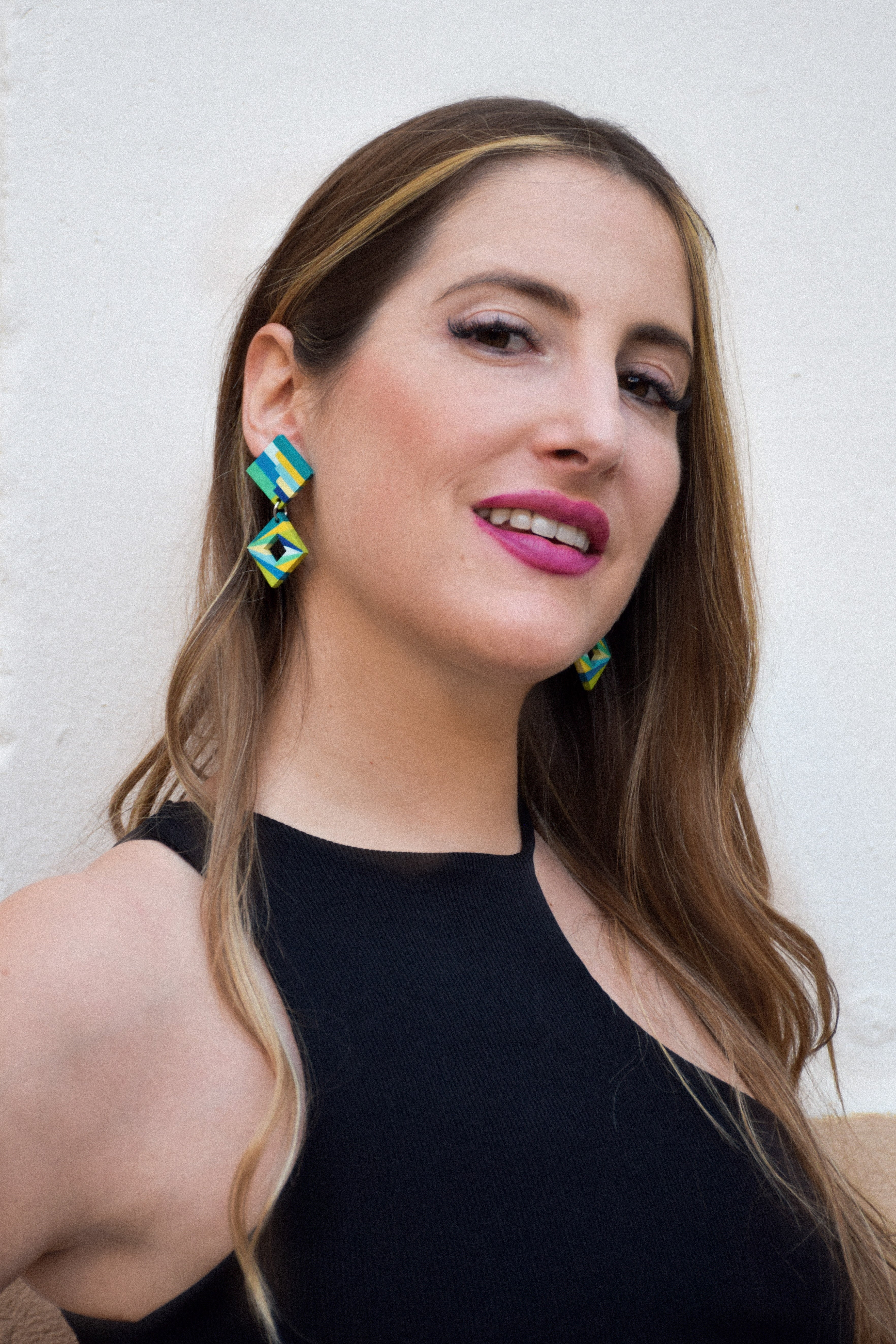 Woman wearing colorful hand-painted earrings against a white background