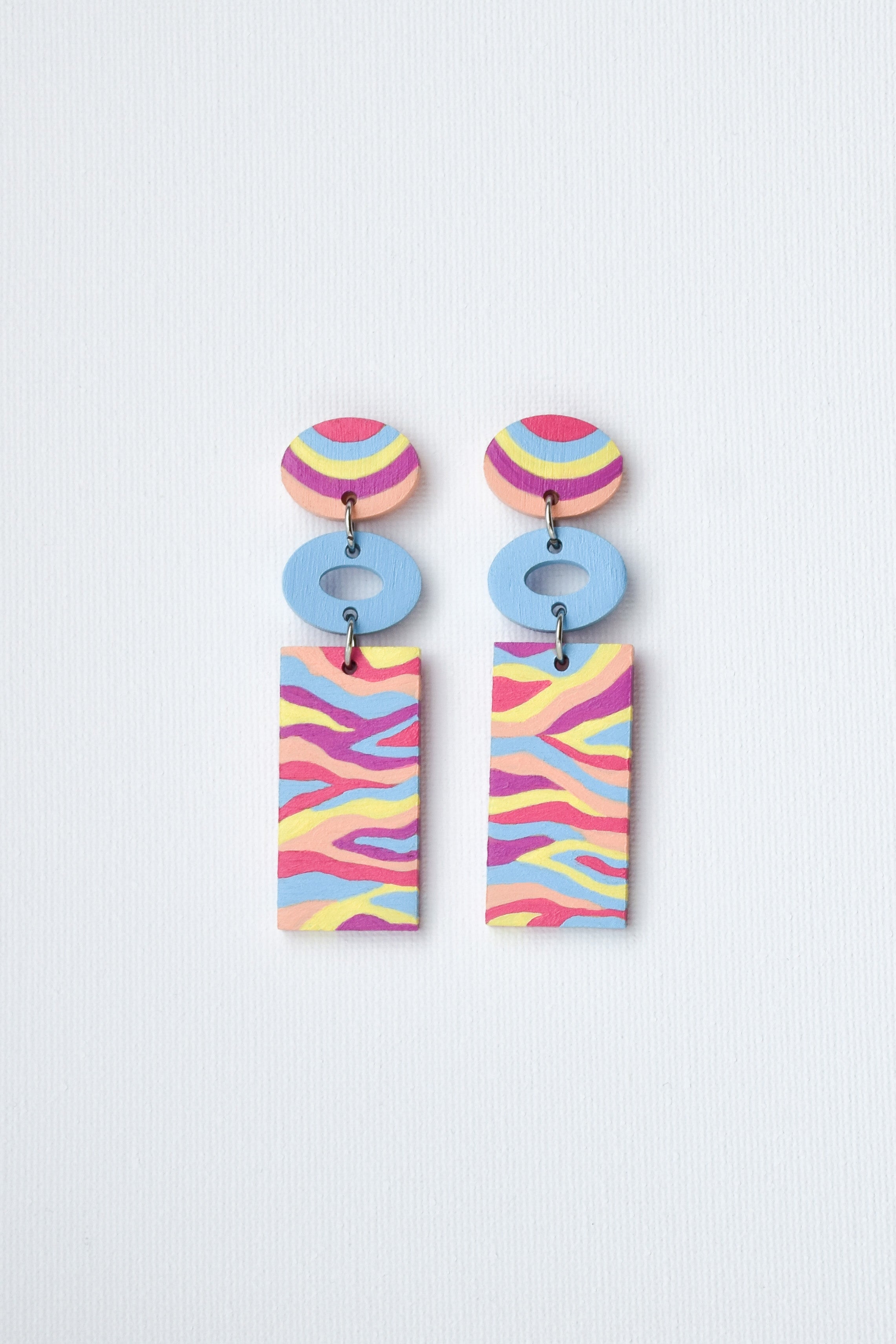 Colorful hand-painted earrings with circular and rectangular designs on a light gray background