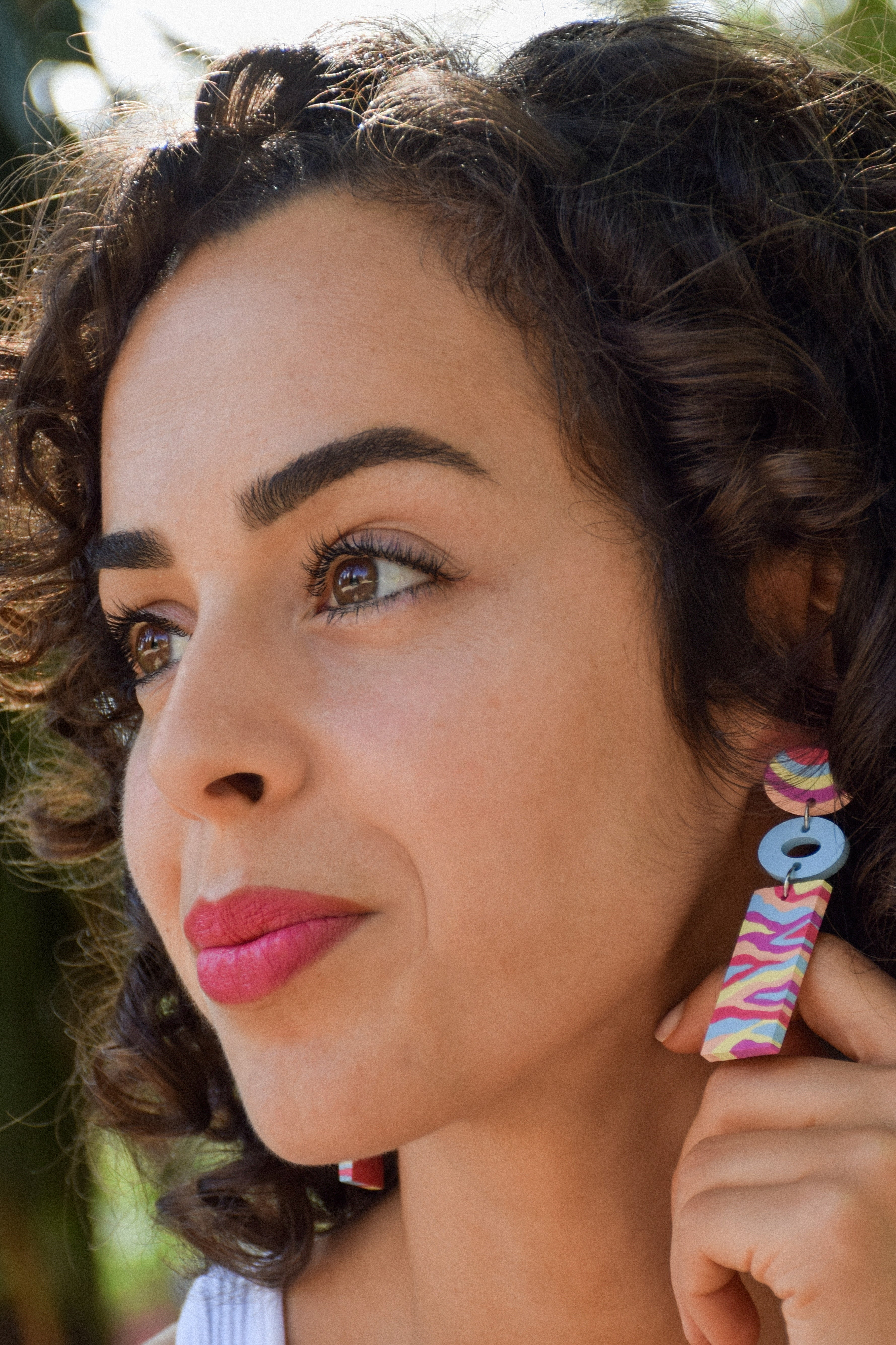 Woman wearing colorful earrings with a blurred natural background