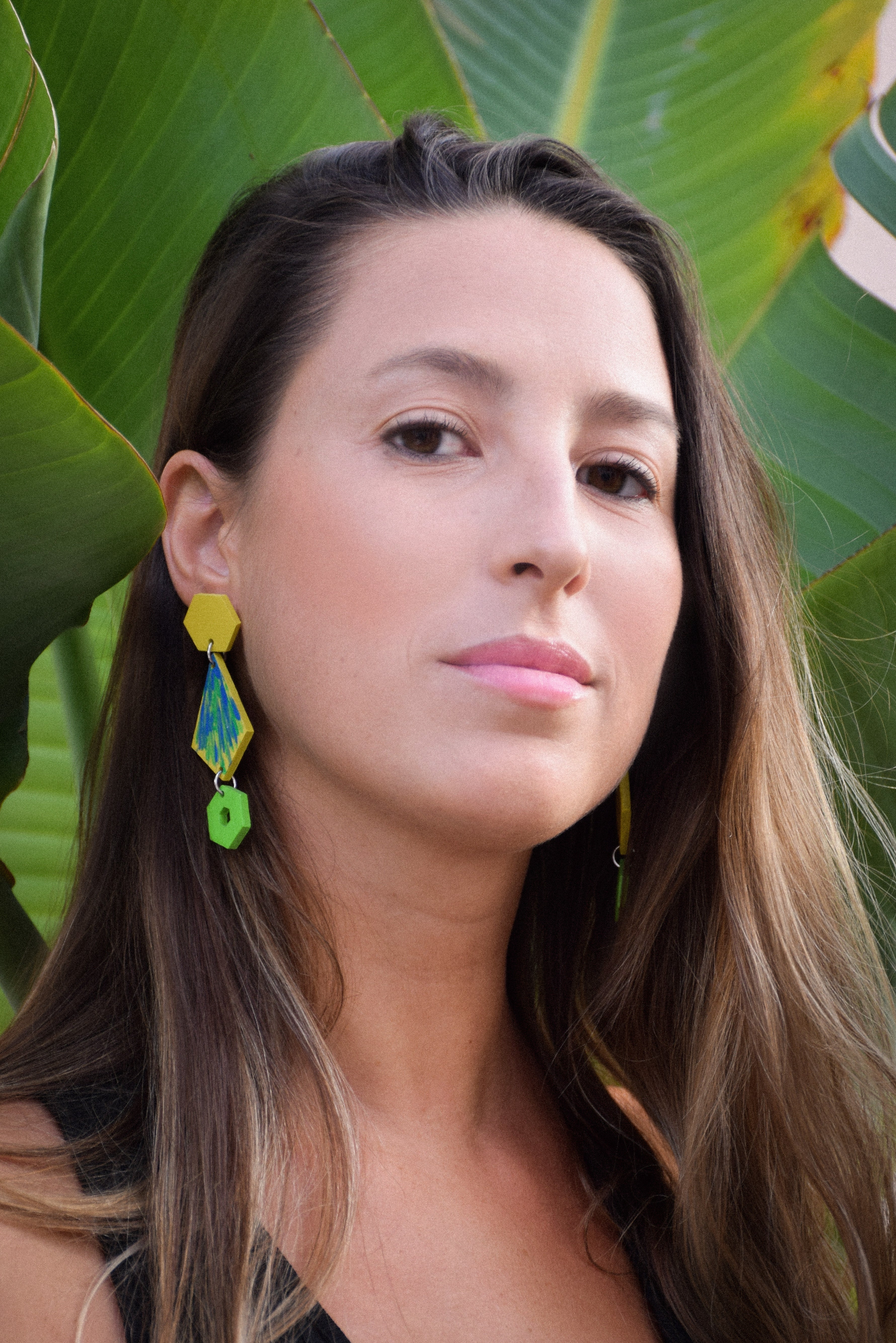 Woman with long hair and colorful earrings against a green leafy background