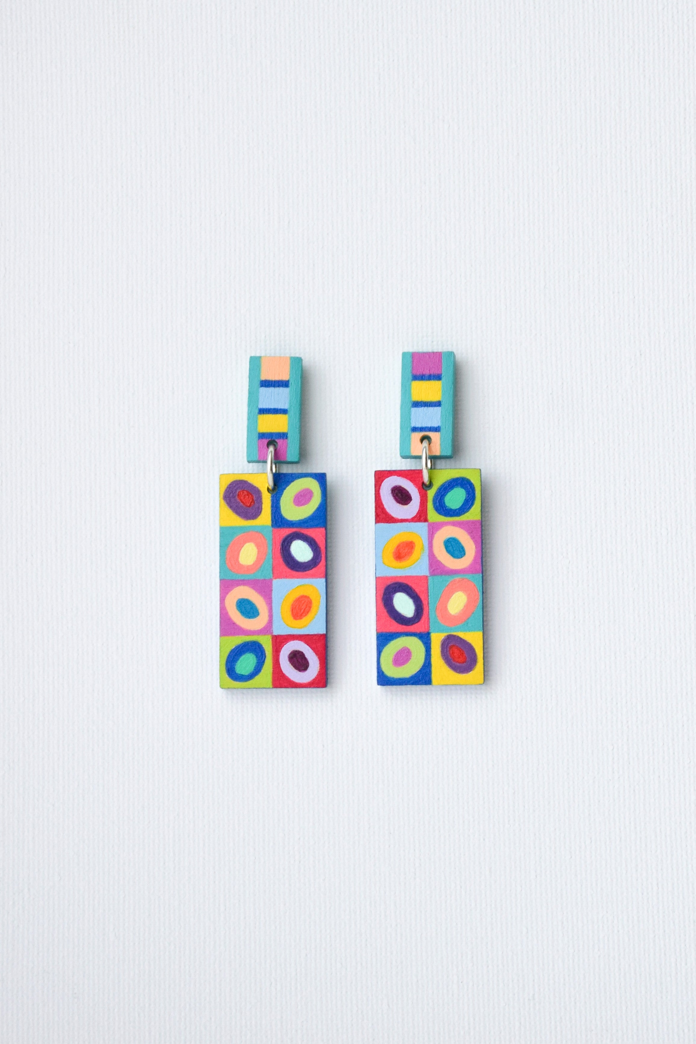 Colorful hand-painted geometric patterned earrings on a light gray background