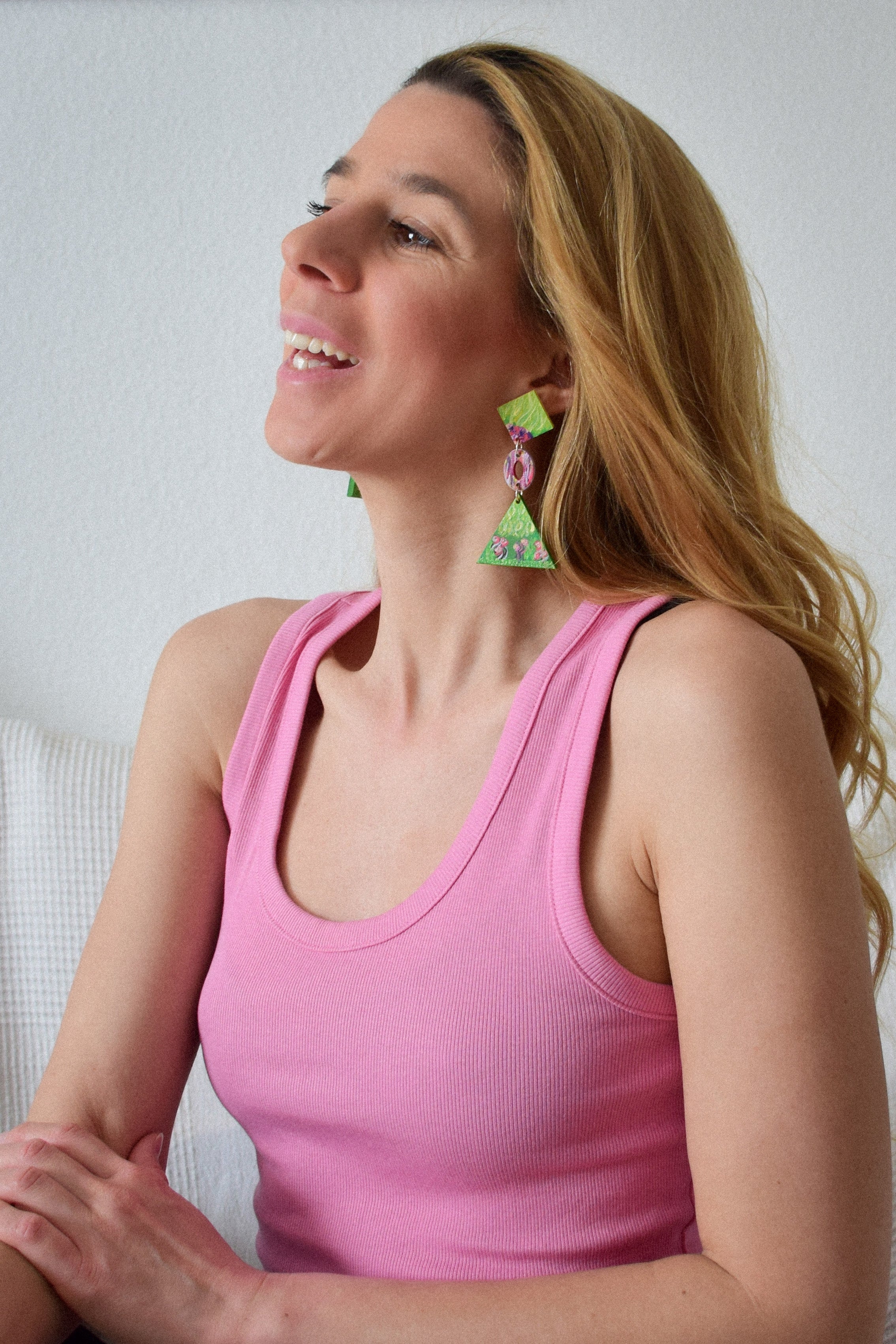 Woman wearing a pink tank top and colorful earrings against a plain background