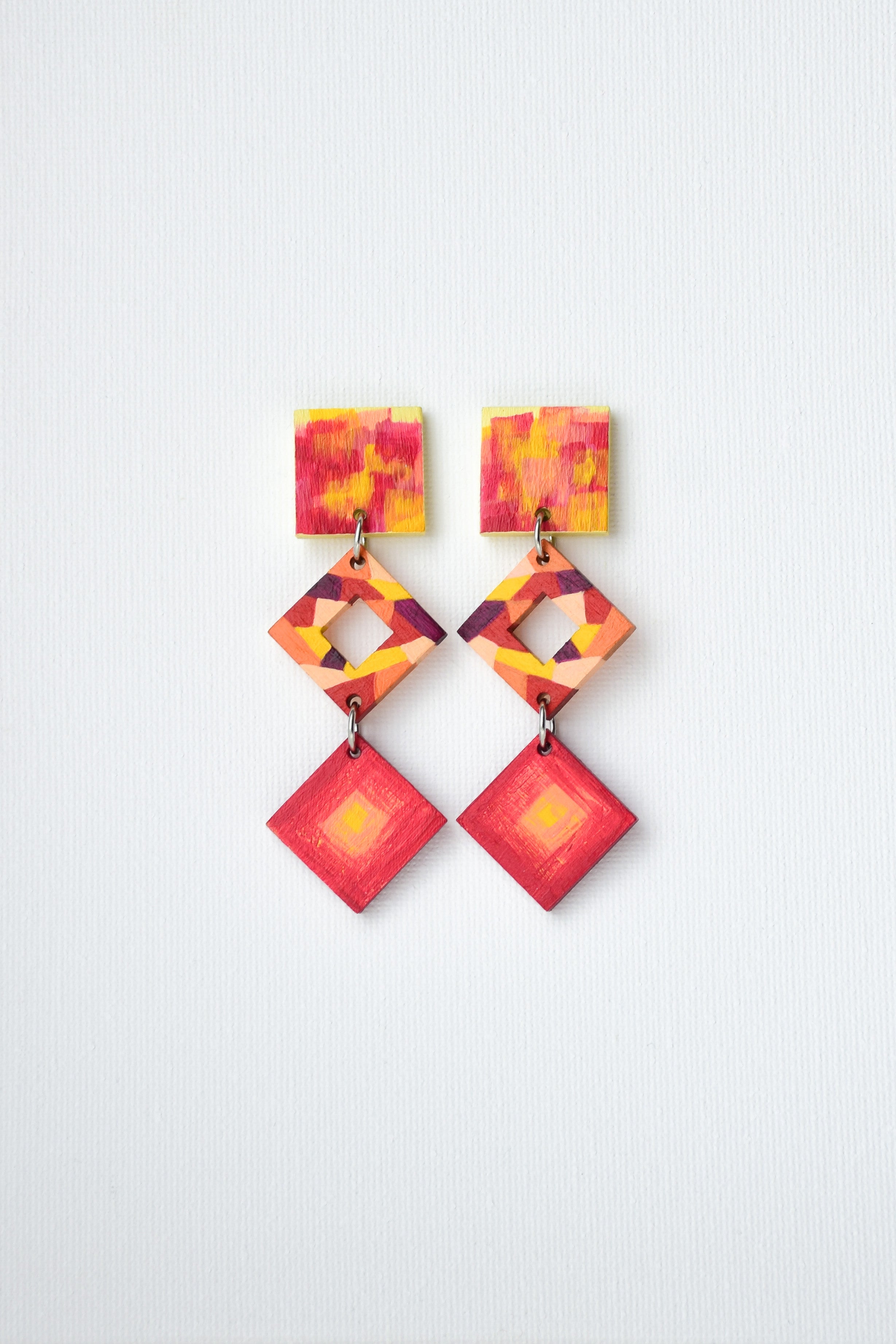 Colorful geometric earrings in red and yellow tones on a light gray background