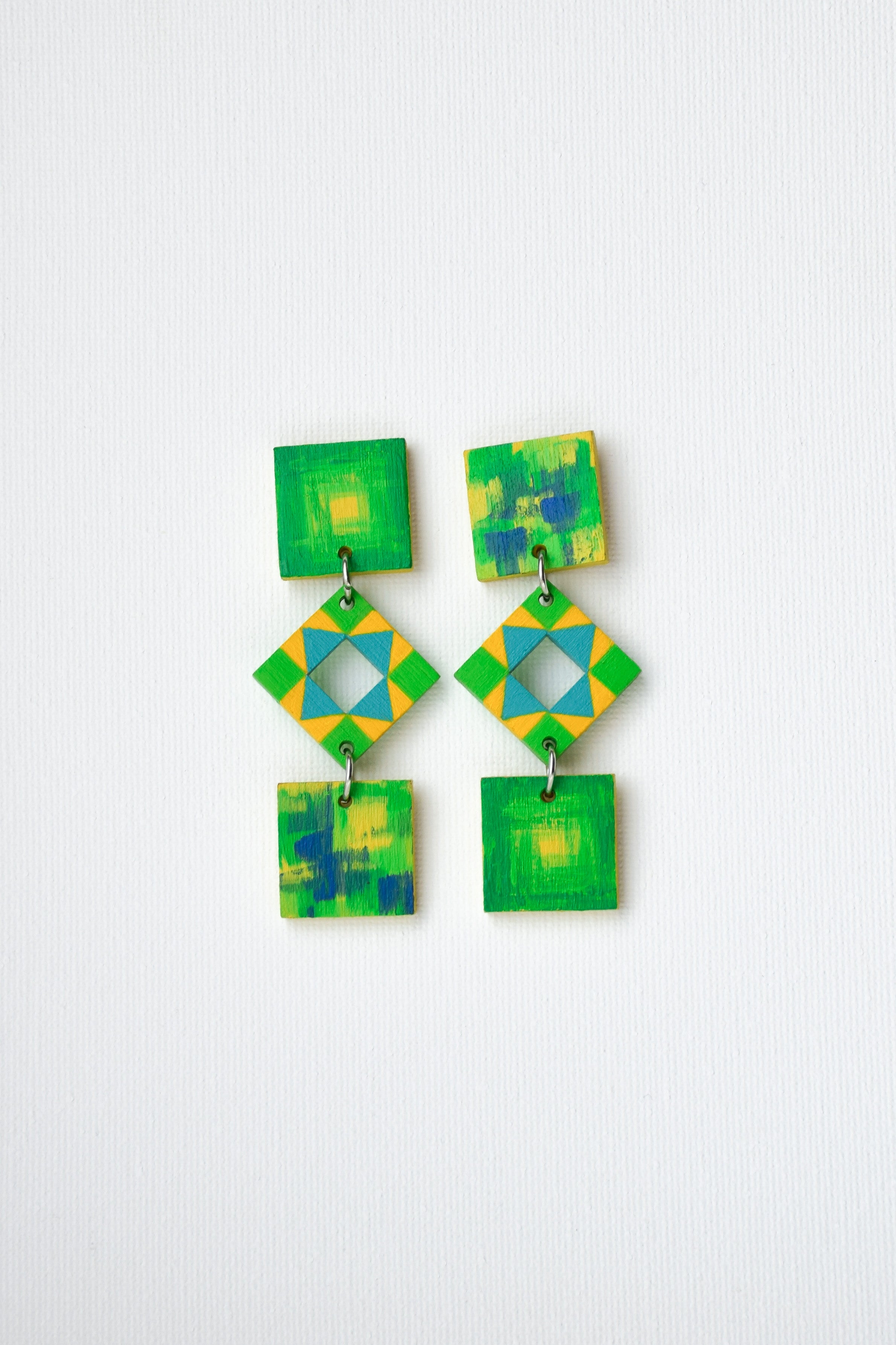 Pair of hand-painted square earrings in green, blue and yellow tones on a white background
