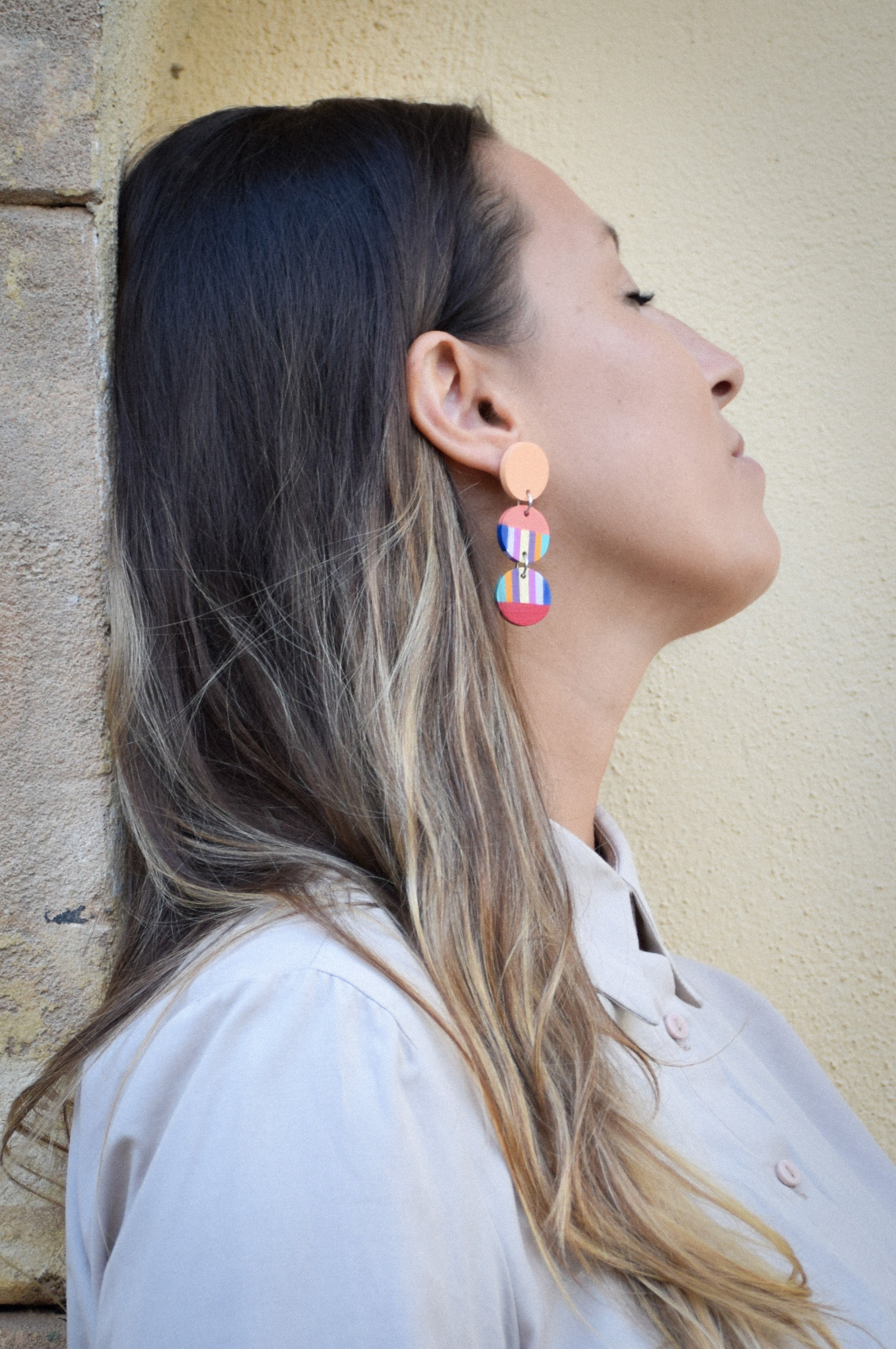 Woman wearing colorful earrings against a neutral wall