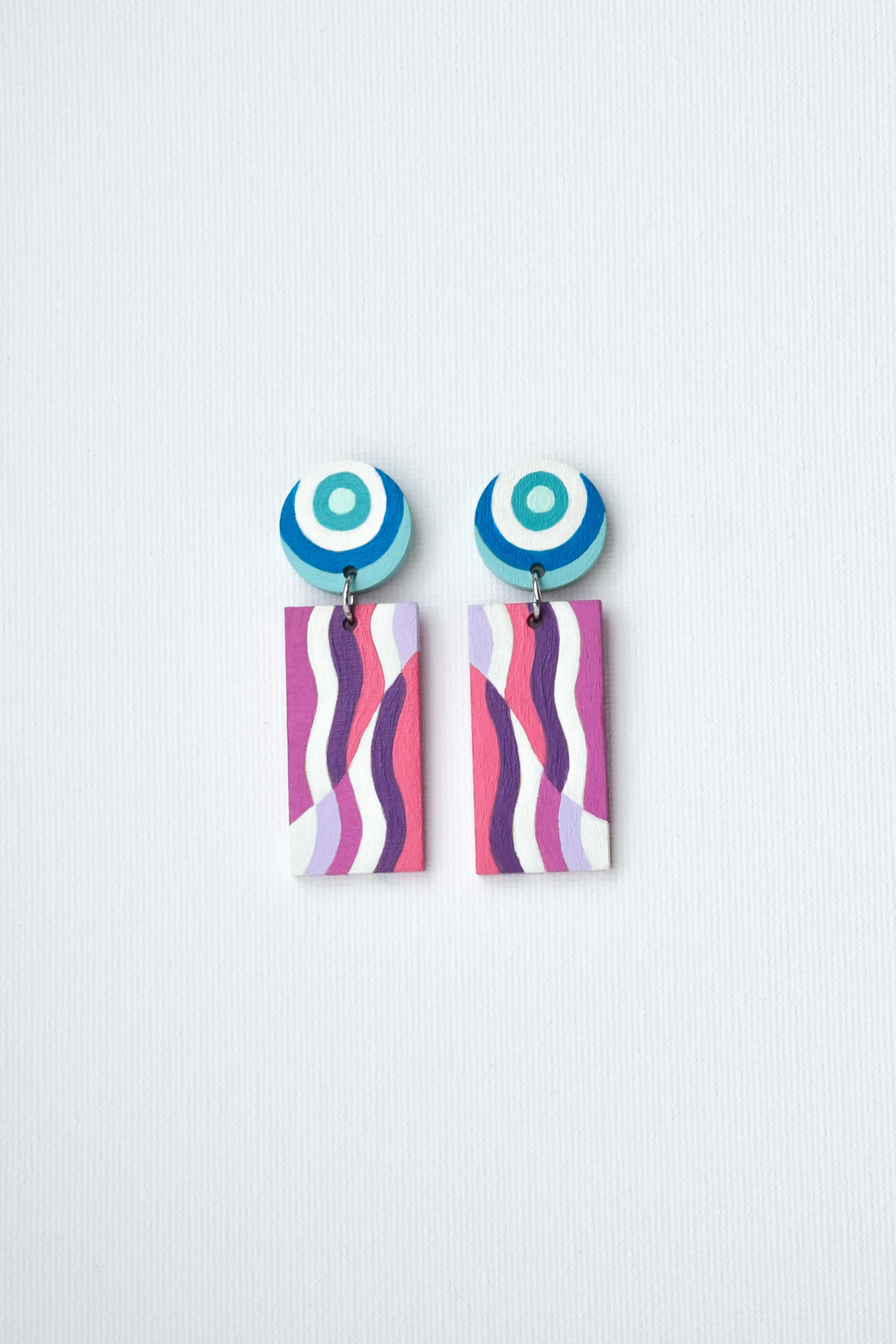 Pair of hand-painted earrings with circular top and striped bottom on a light gray background