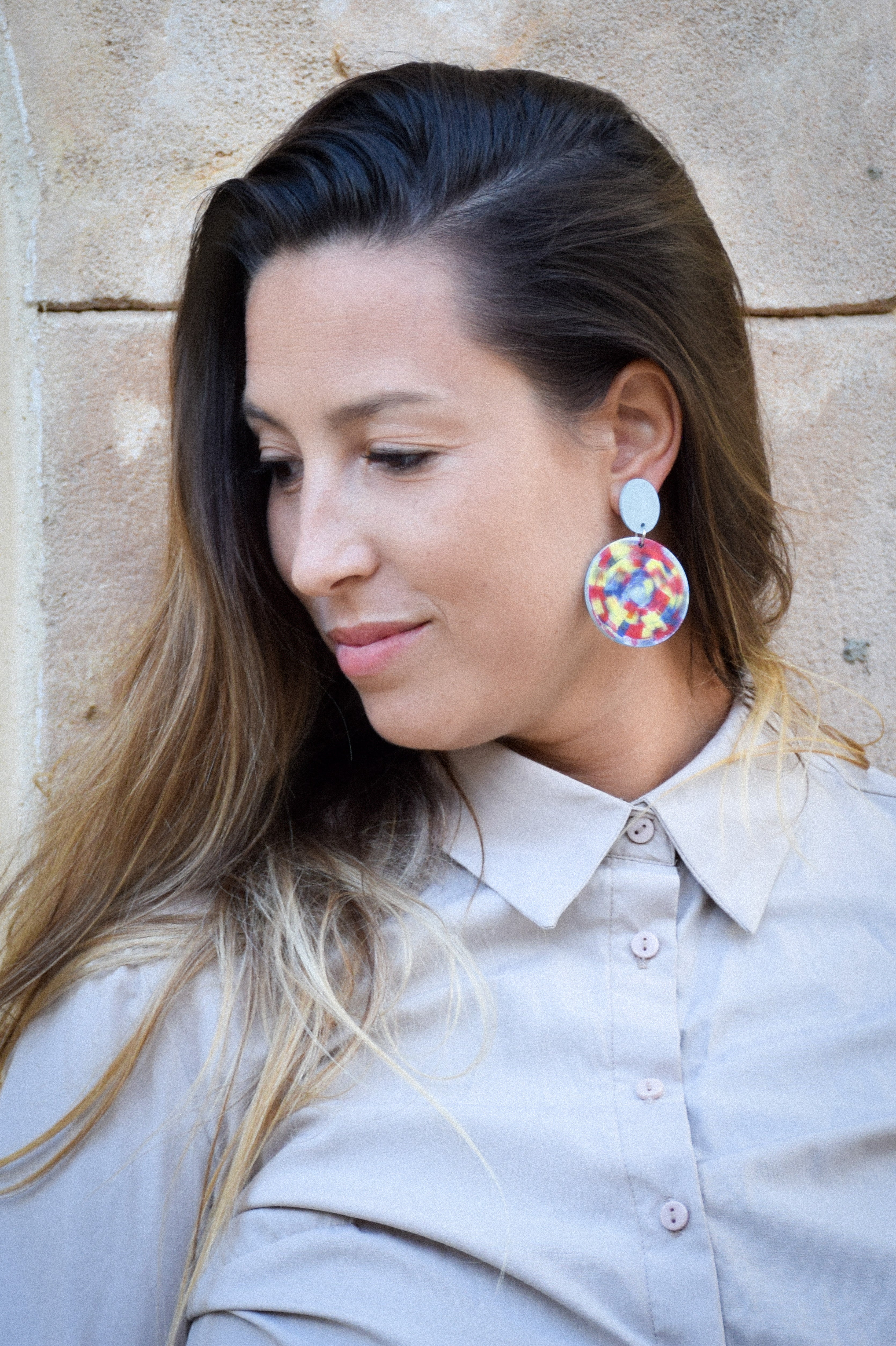 Woman wearing colorful earrings against a stone wall background