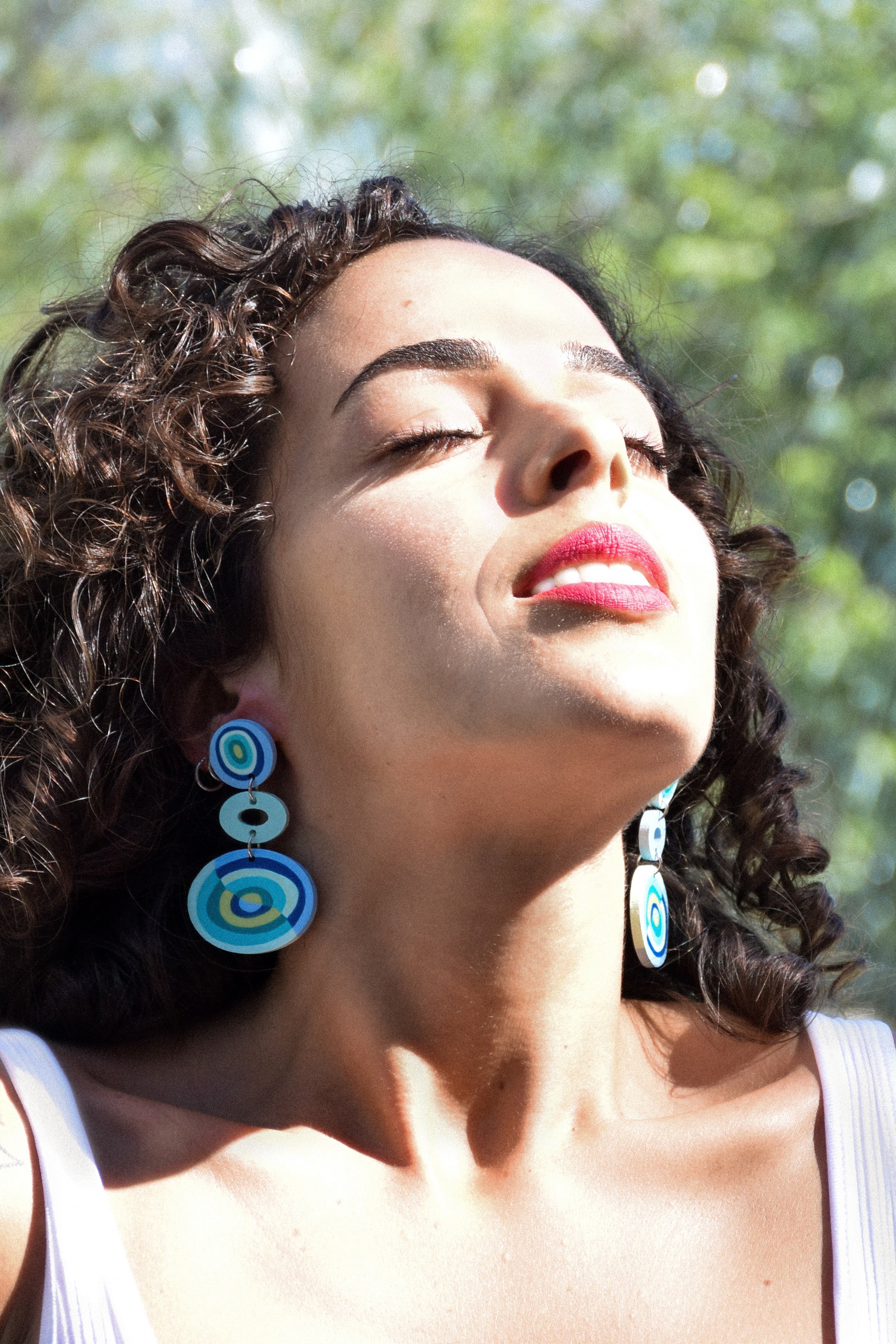 Woman wearing blue circular earrings with a blurred green background