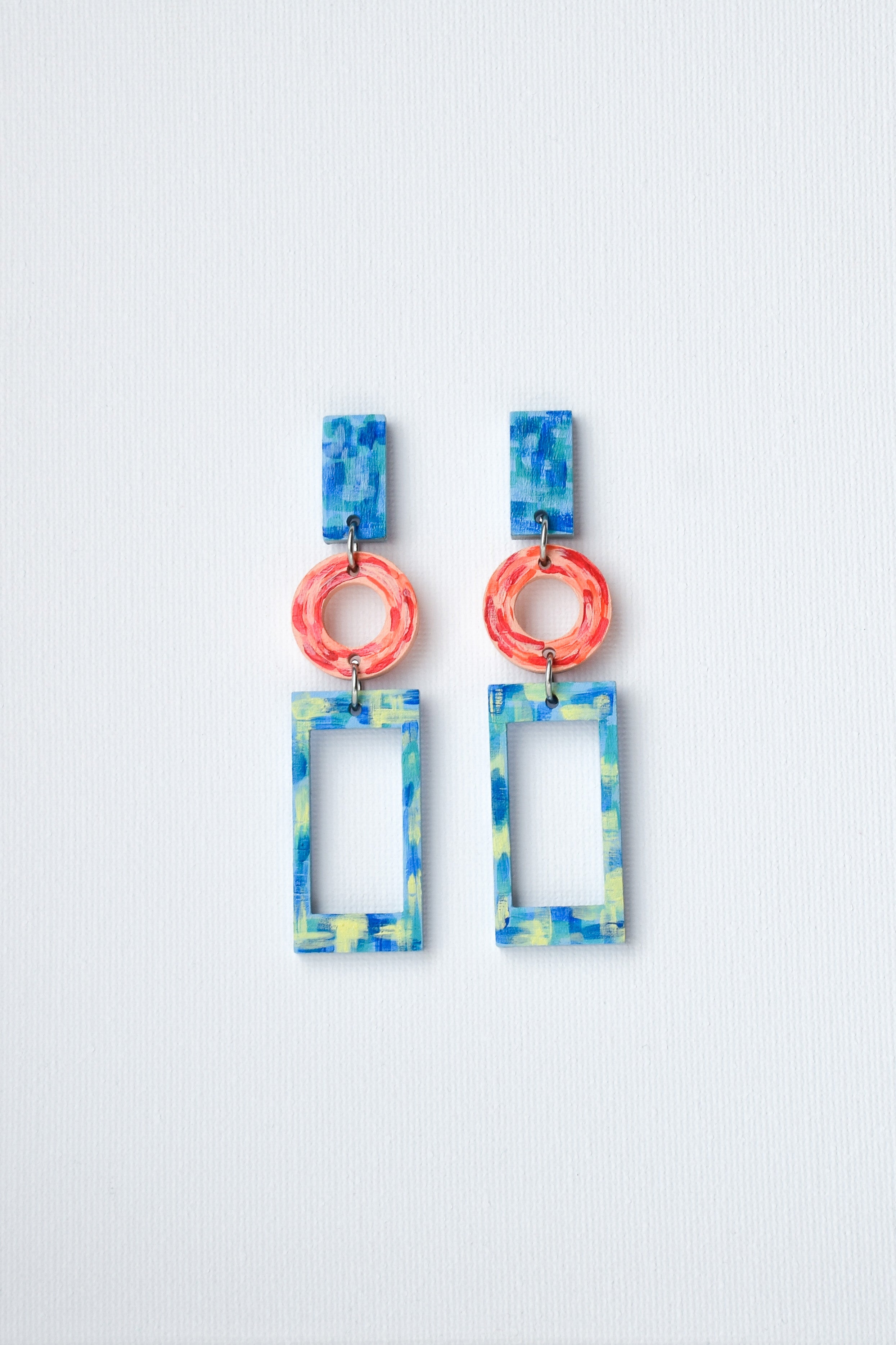 Colorful hand-painted earrings with geometric designs on a light gray background