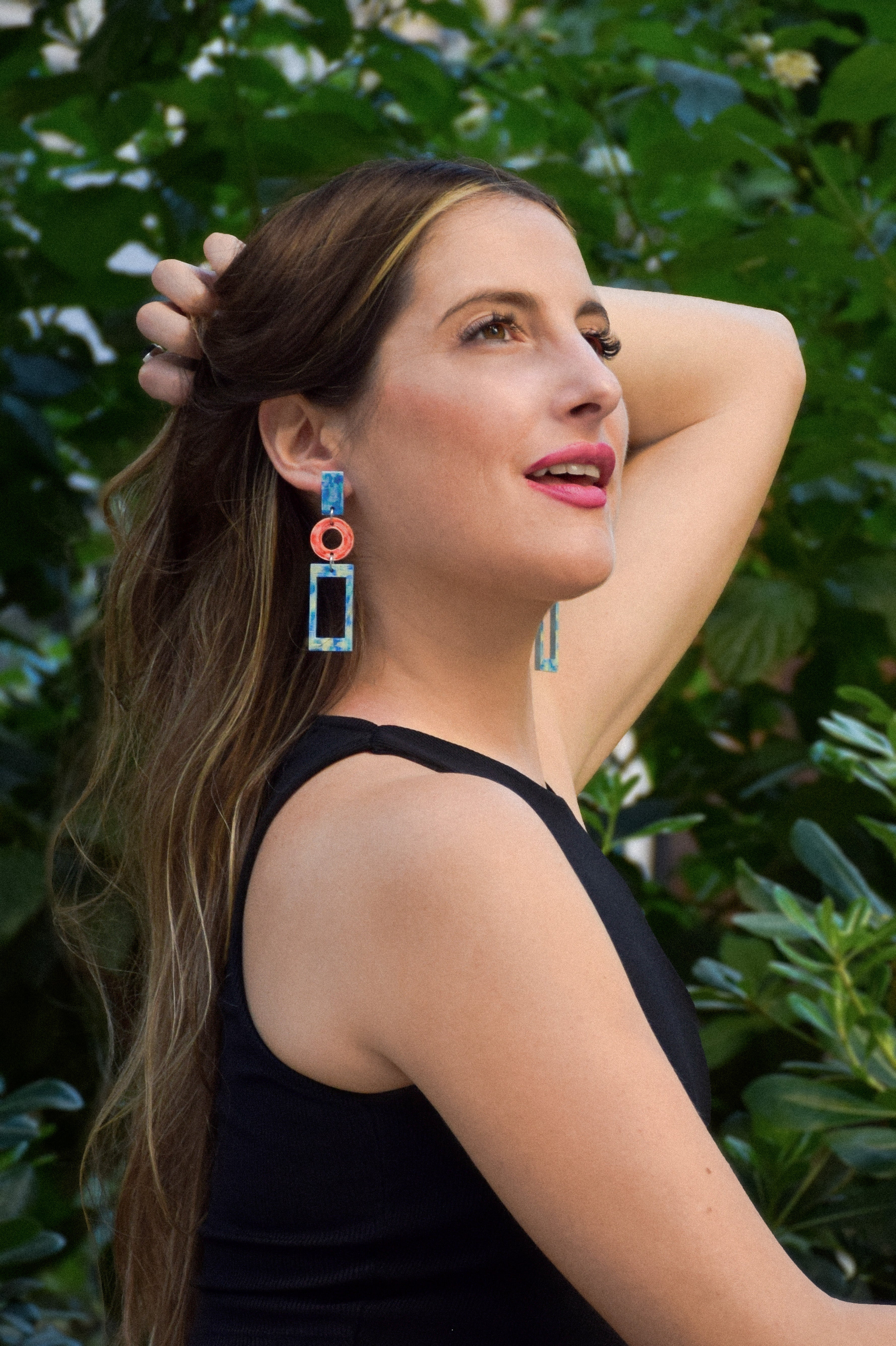 Woman with colorful earrings posing outdoors against a green leafy background