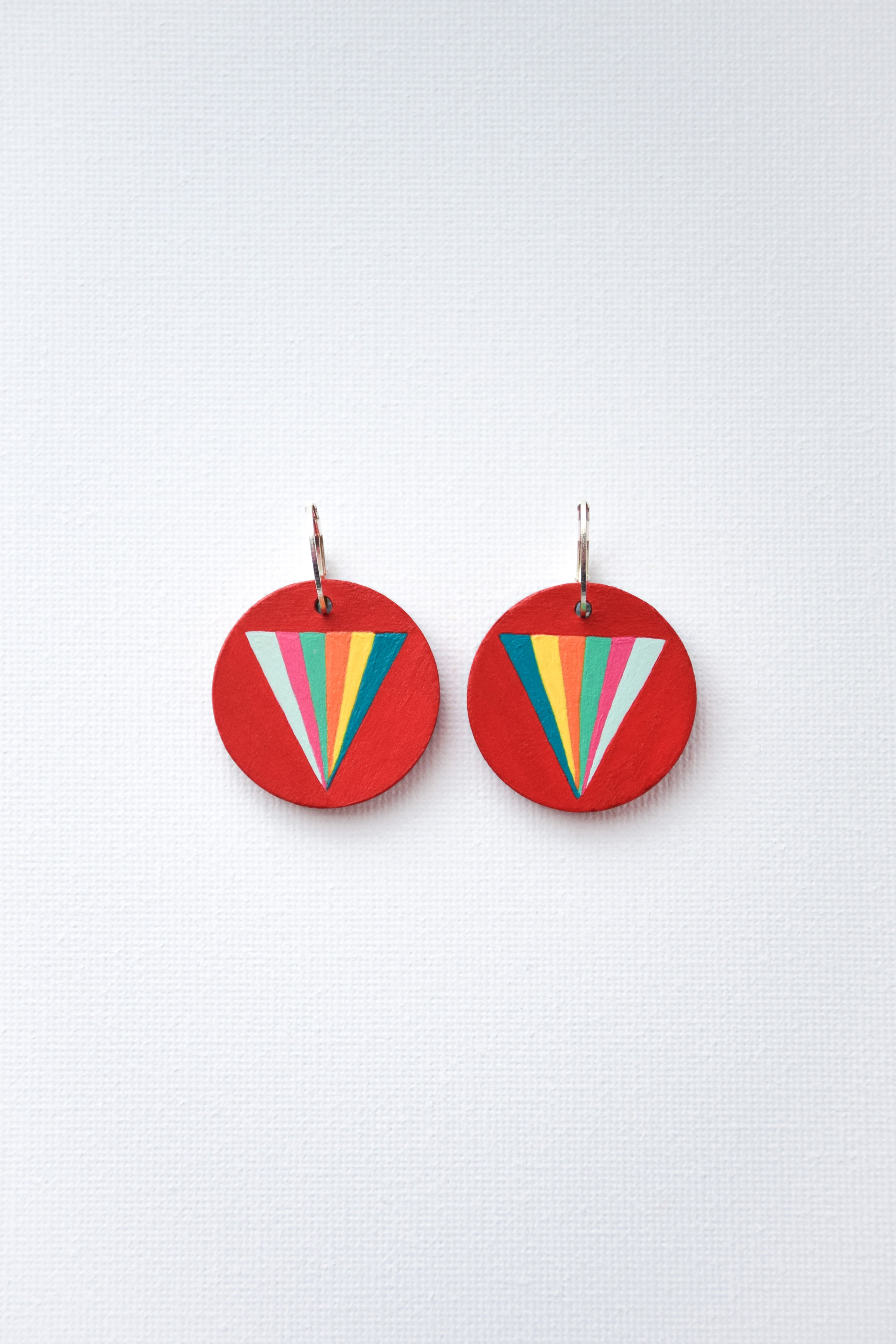 Red hand-painted circular earrings with colorful triangle design and sterling silver hoops on a white background