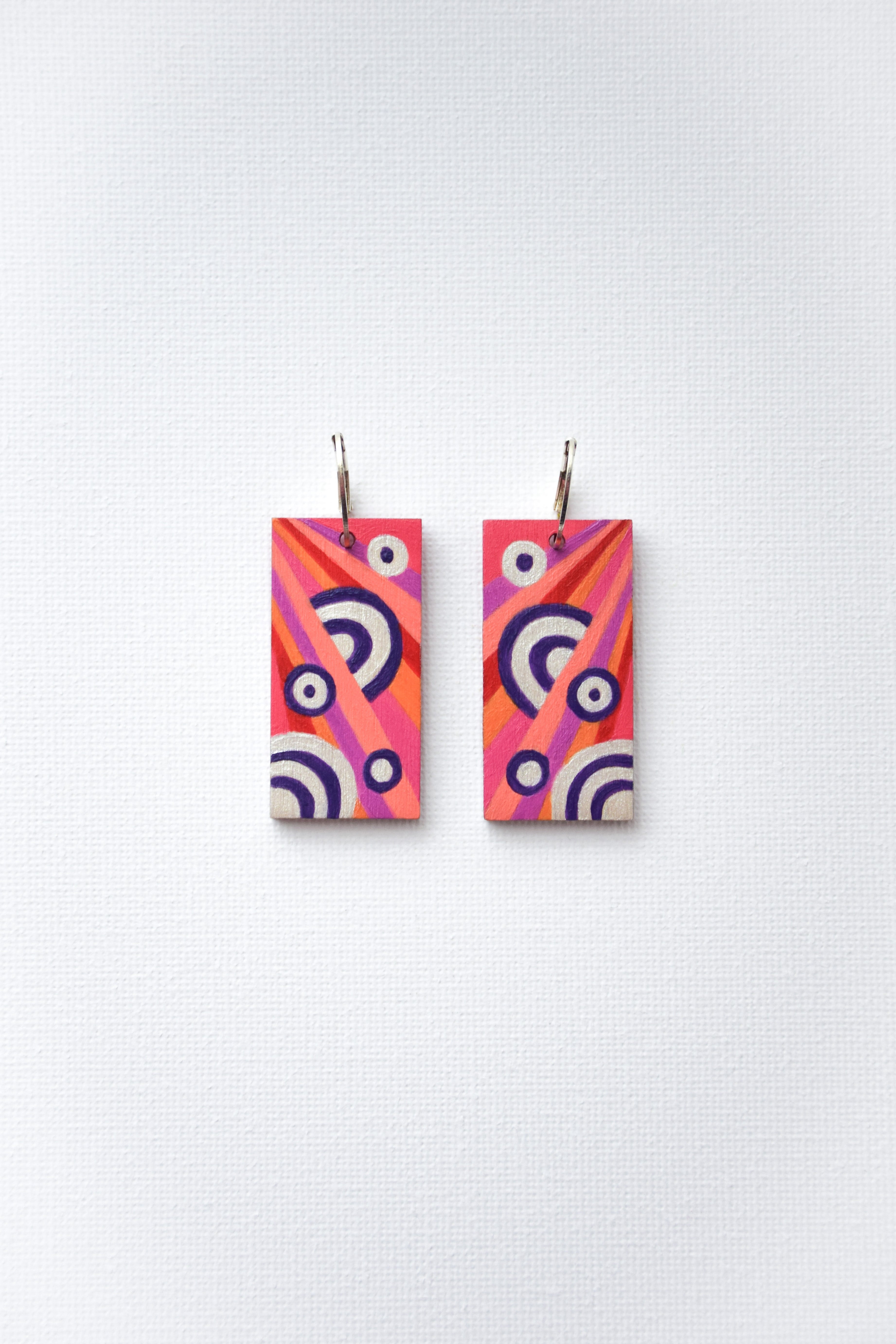 Pair of hand-painted colorful rectangular earrings with sterling silver hoops on a white background