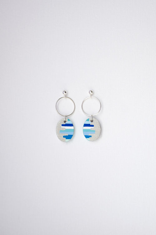 Pair of hand-painted earrings with blue and white striped designs and sterling silver hoops on a light gray background