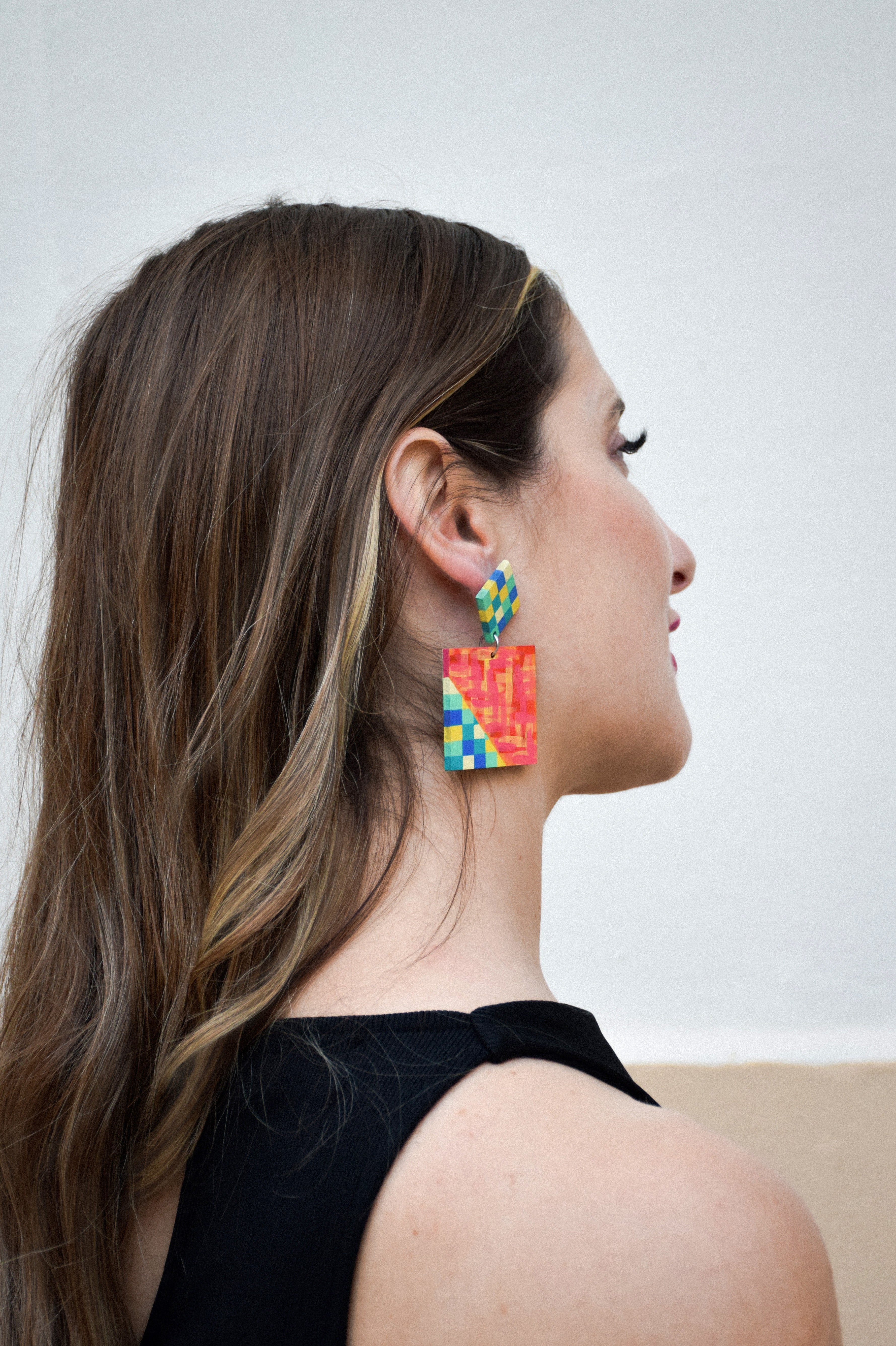 Woman wearing colorful square earrings against a plain background