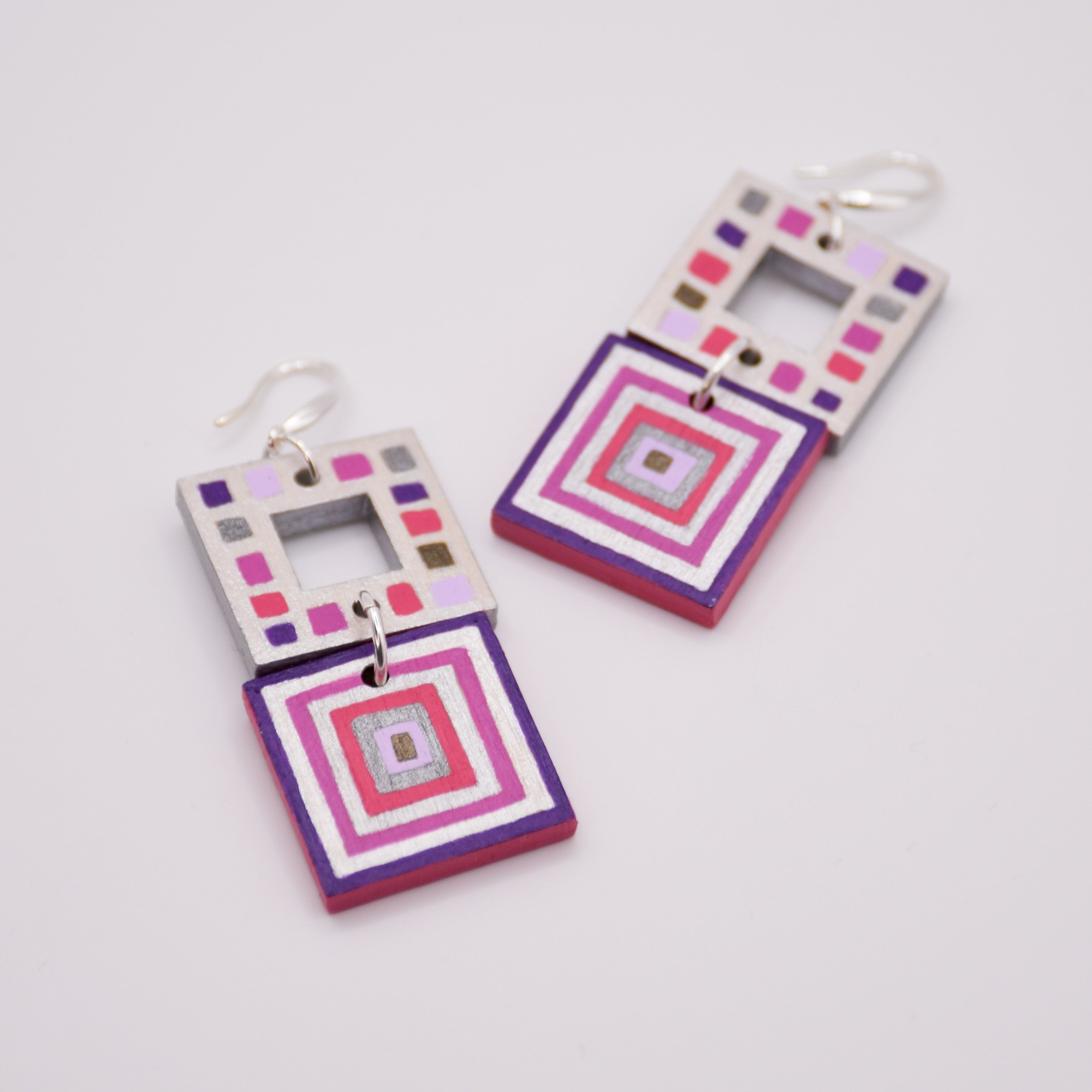 Pair of square-shaped earrings with colorful geometric pattern on a light gray background