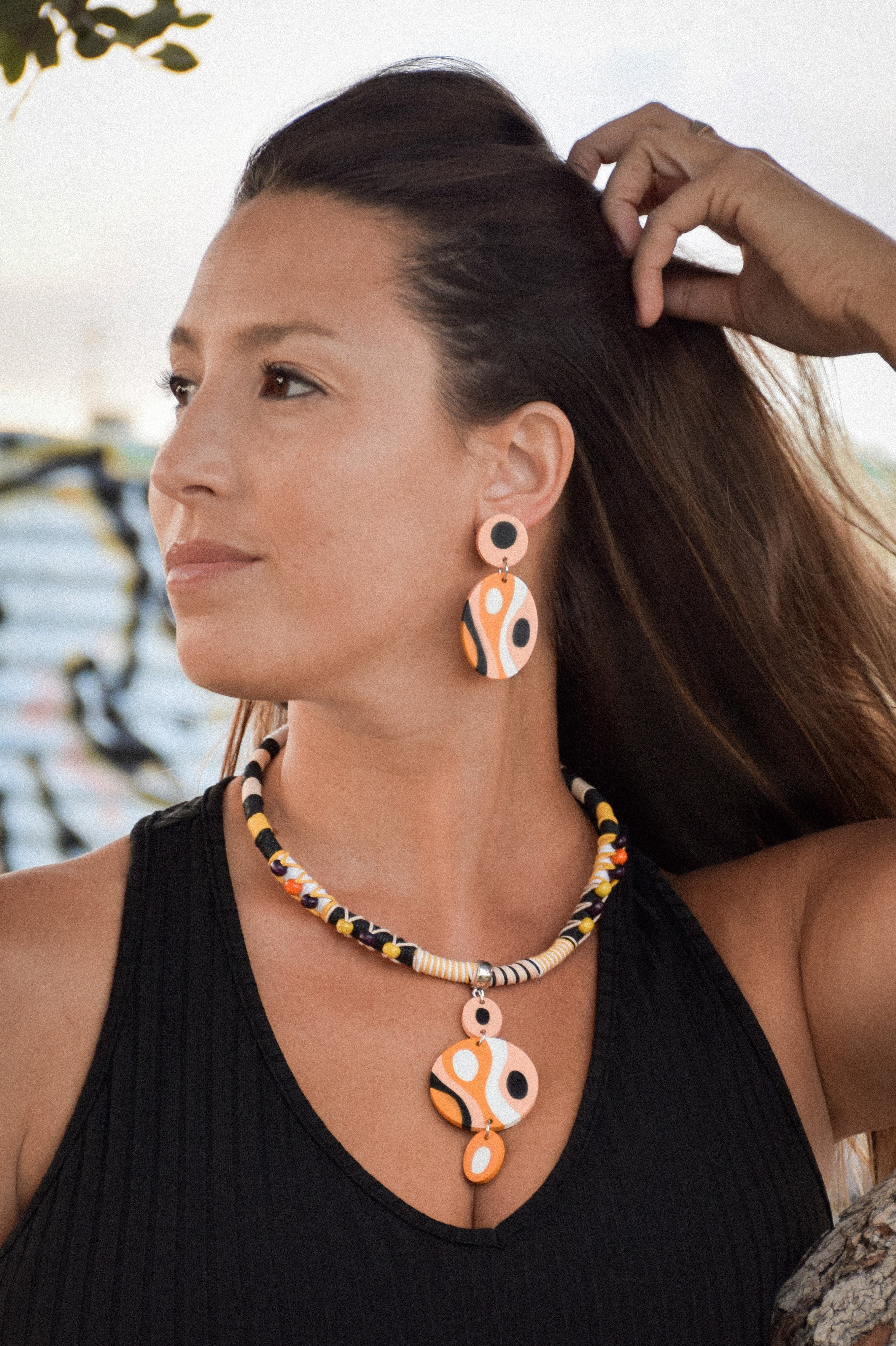 Woman wearing a black sleeveless top with a colorful necklace and earrings outdoors.