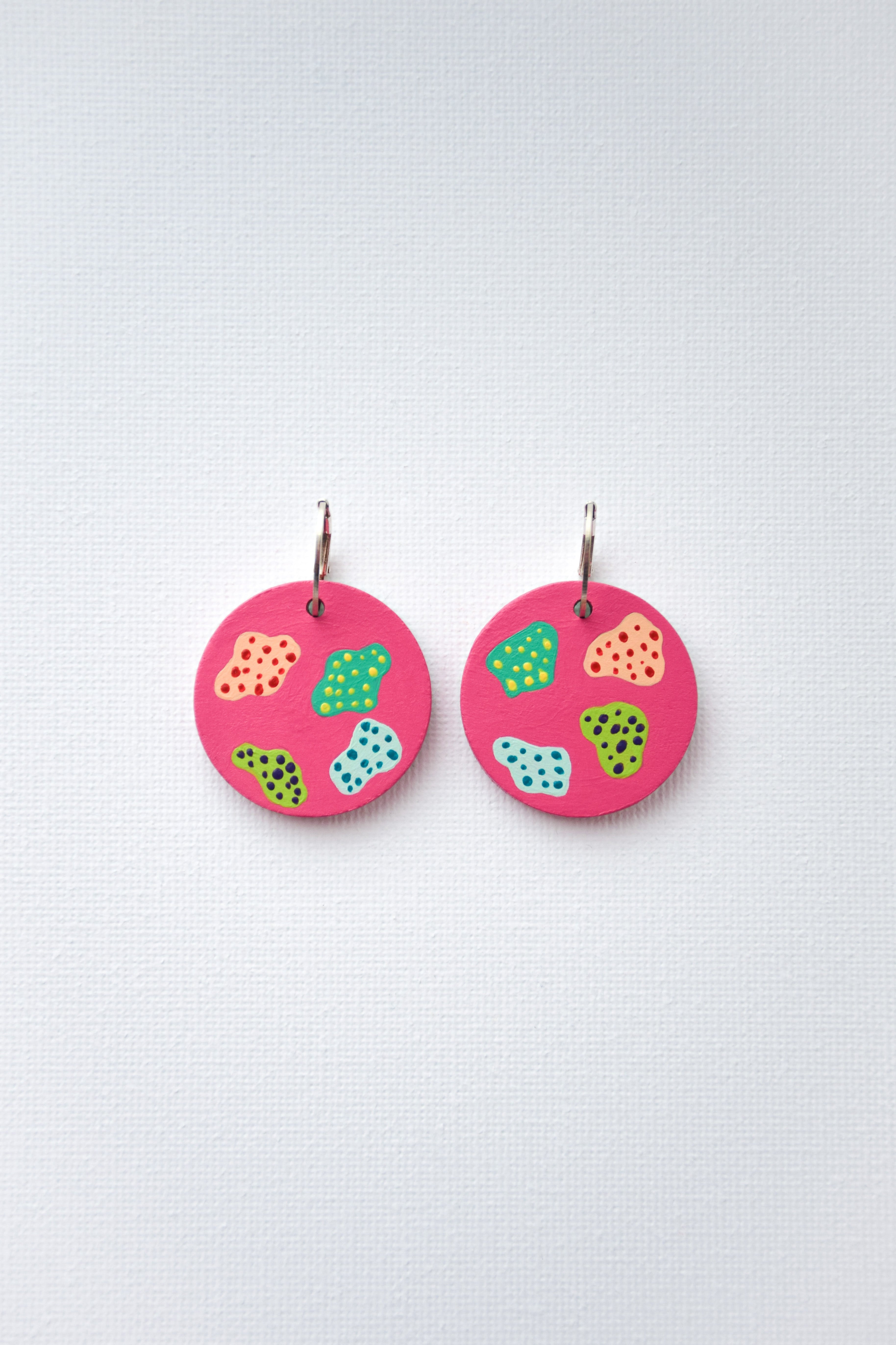 Hand-painted pink earrings with colorful patterns and sterling silver hoops on a light gray background