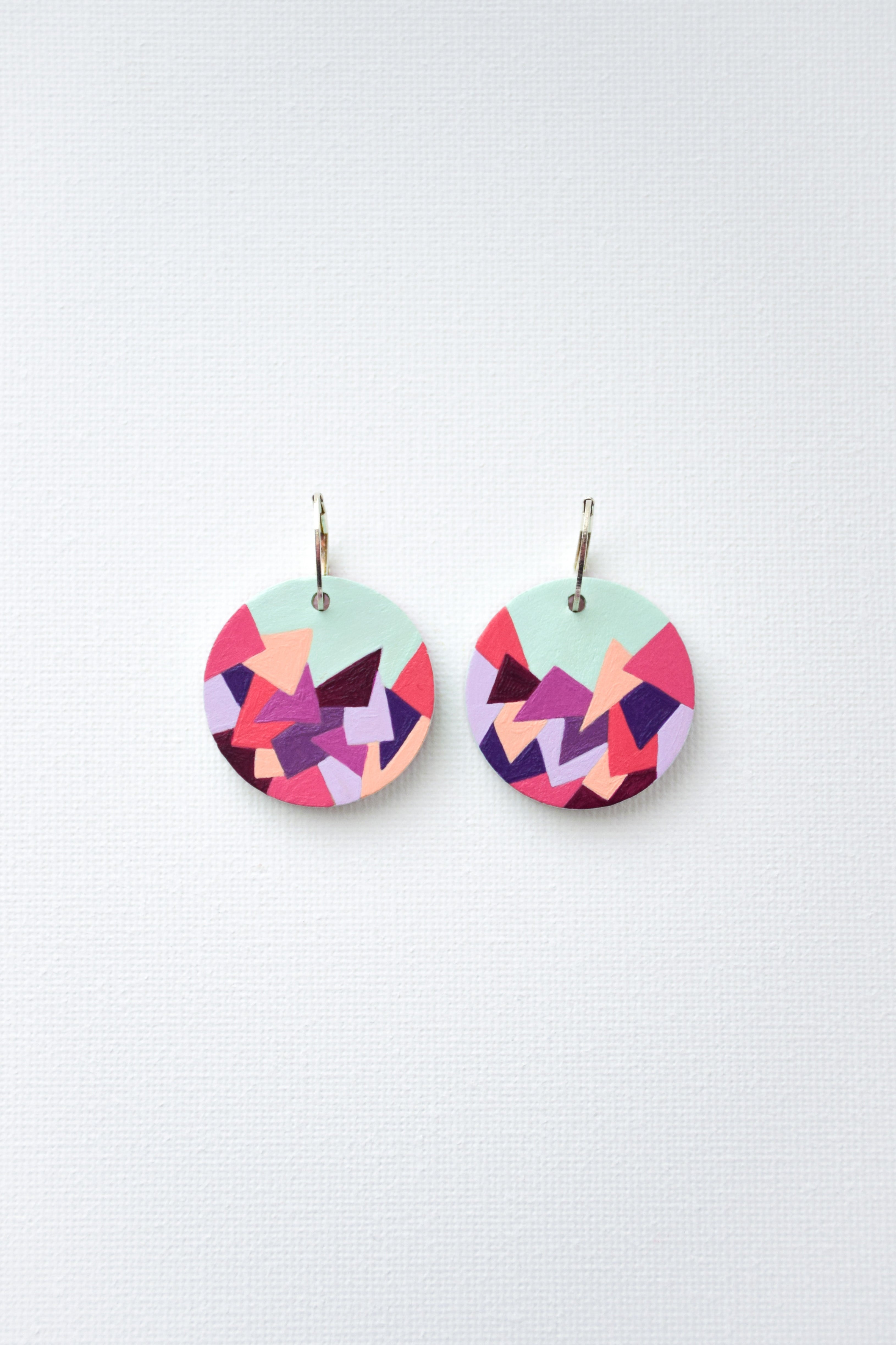 Colorful hand-painted geometric patterned earrings with sterling silver hoops on a light gray background