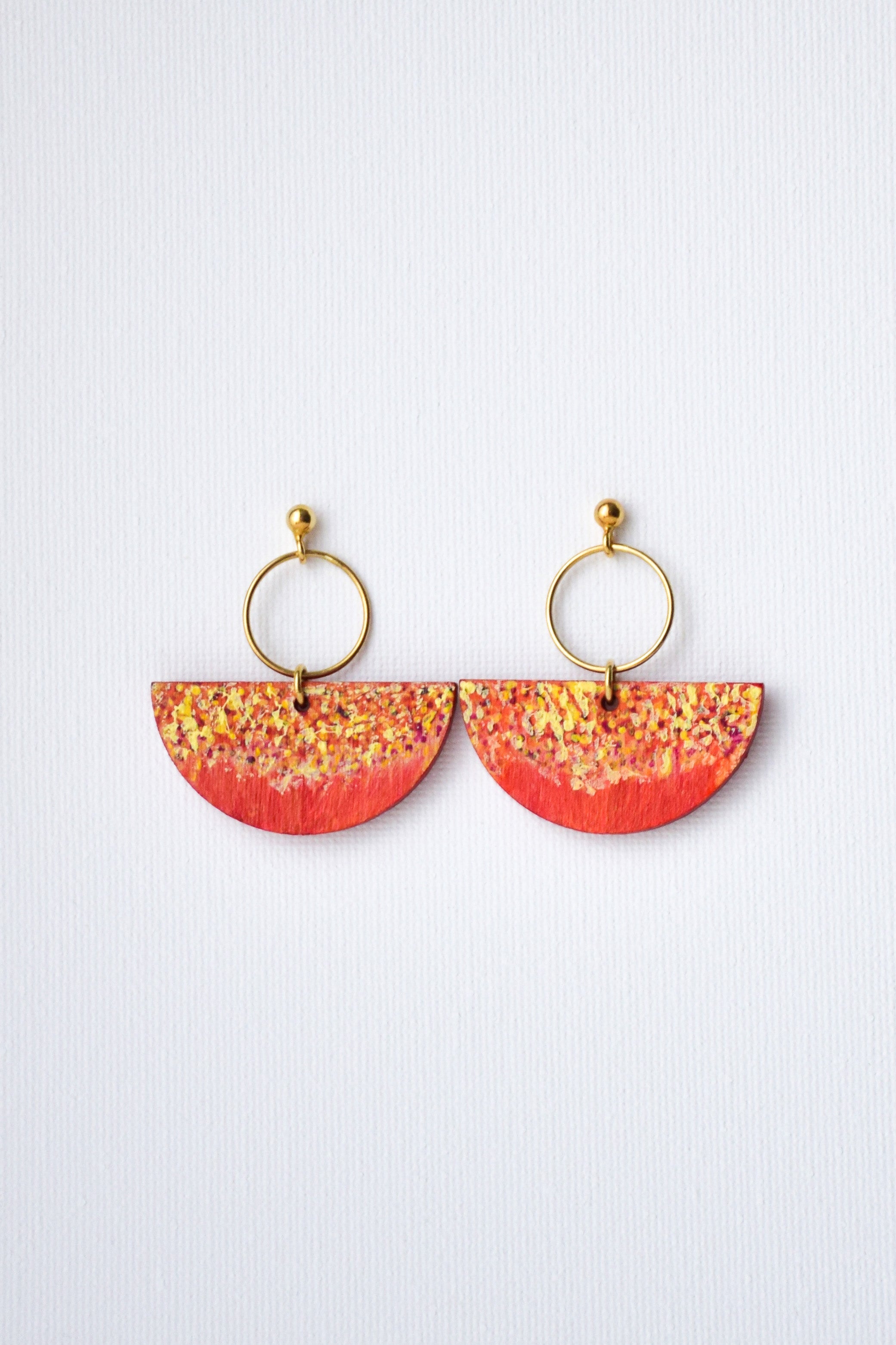 Pair of earrings with red and yellow half-circle design and gold hoops on a white background
