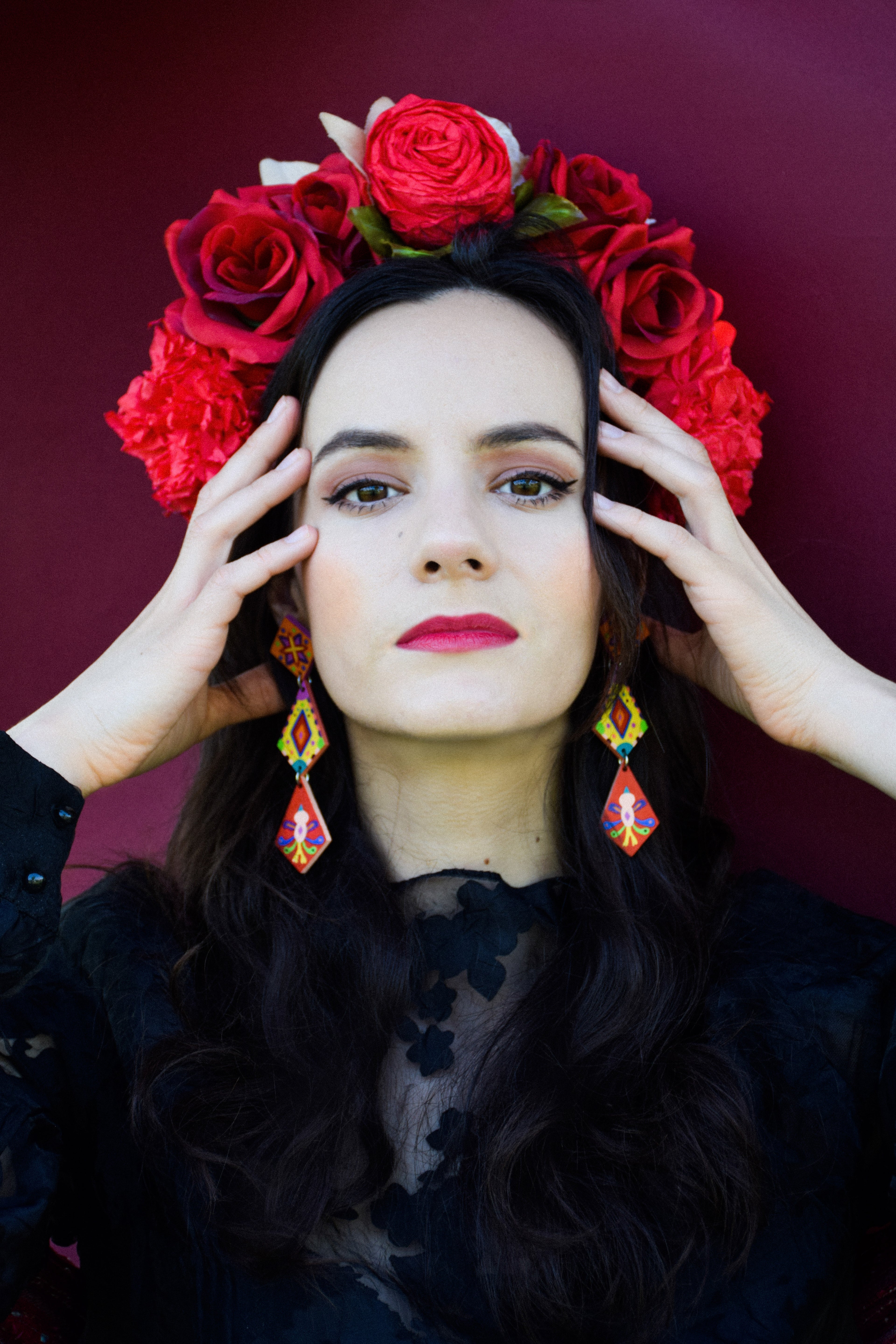 Woman wearing a floral headpiece with red roses and colorful earrings against a dark background