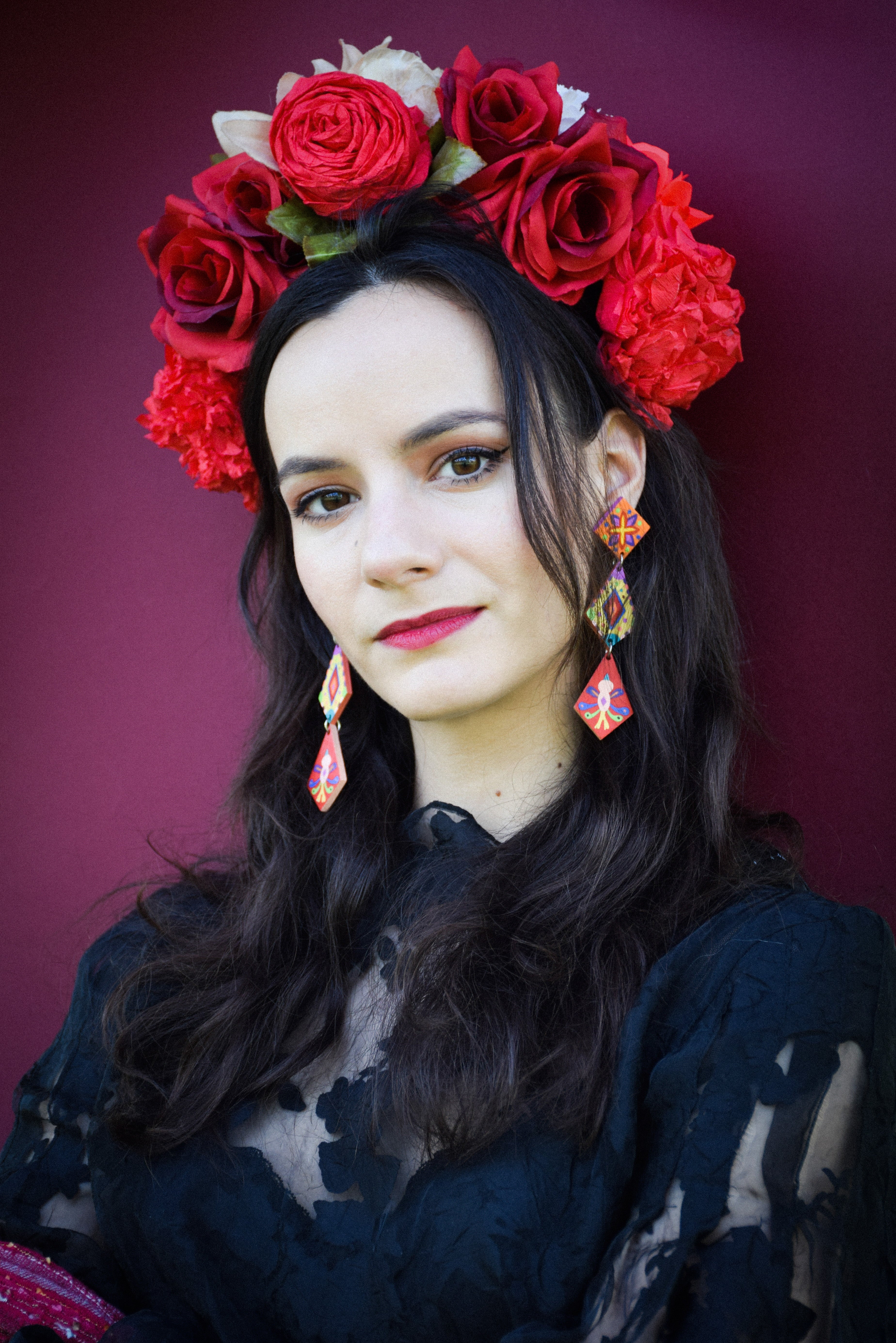 Woman wearing a floral headpiece with red roses and colorful earrings against a dark background