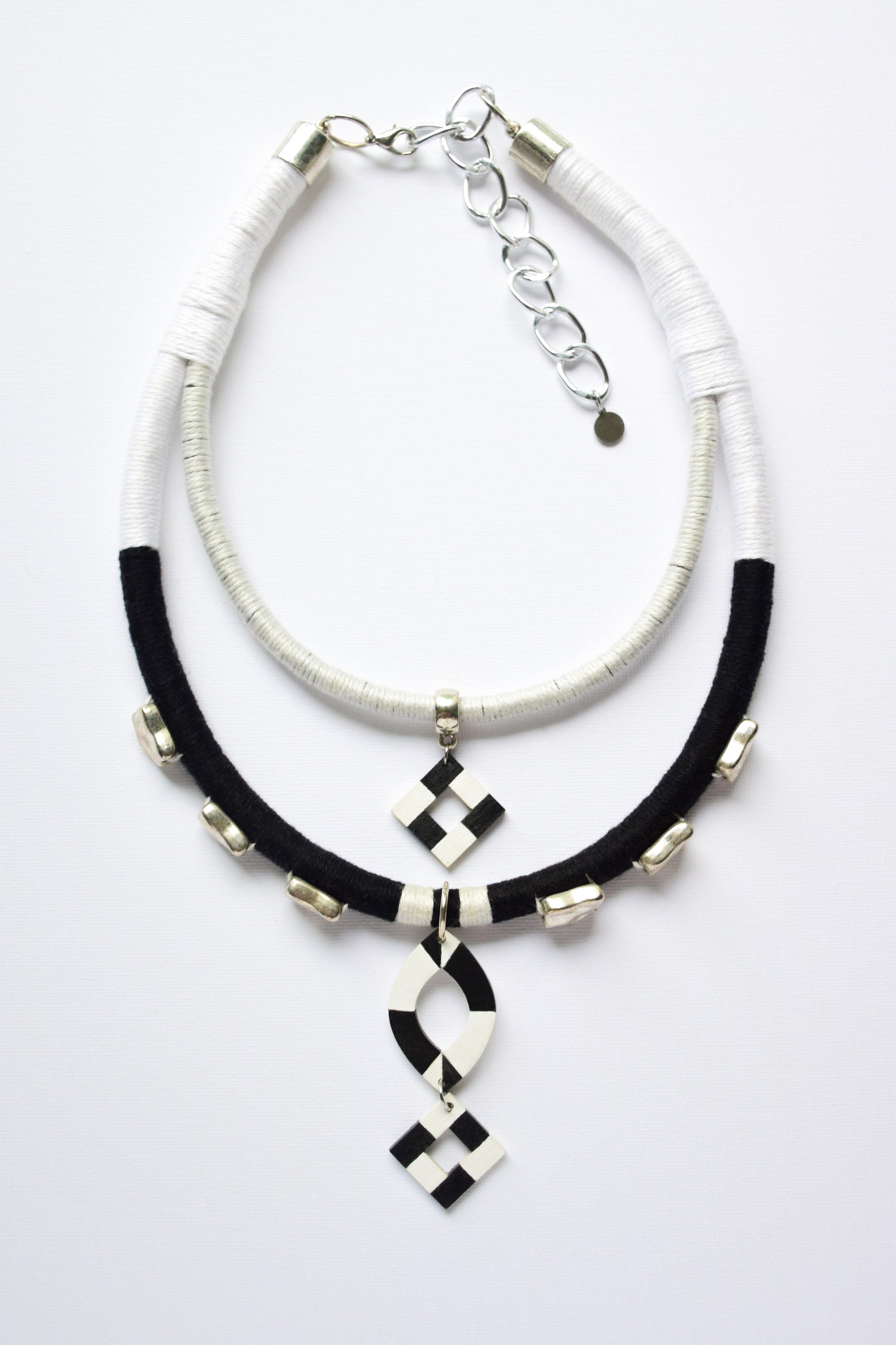 Necklace with black and white cord and geometric pendant on a light gray background