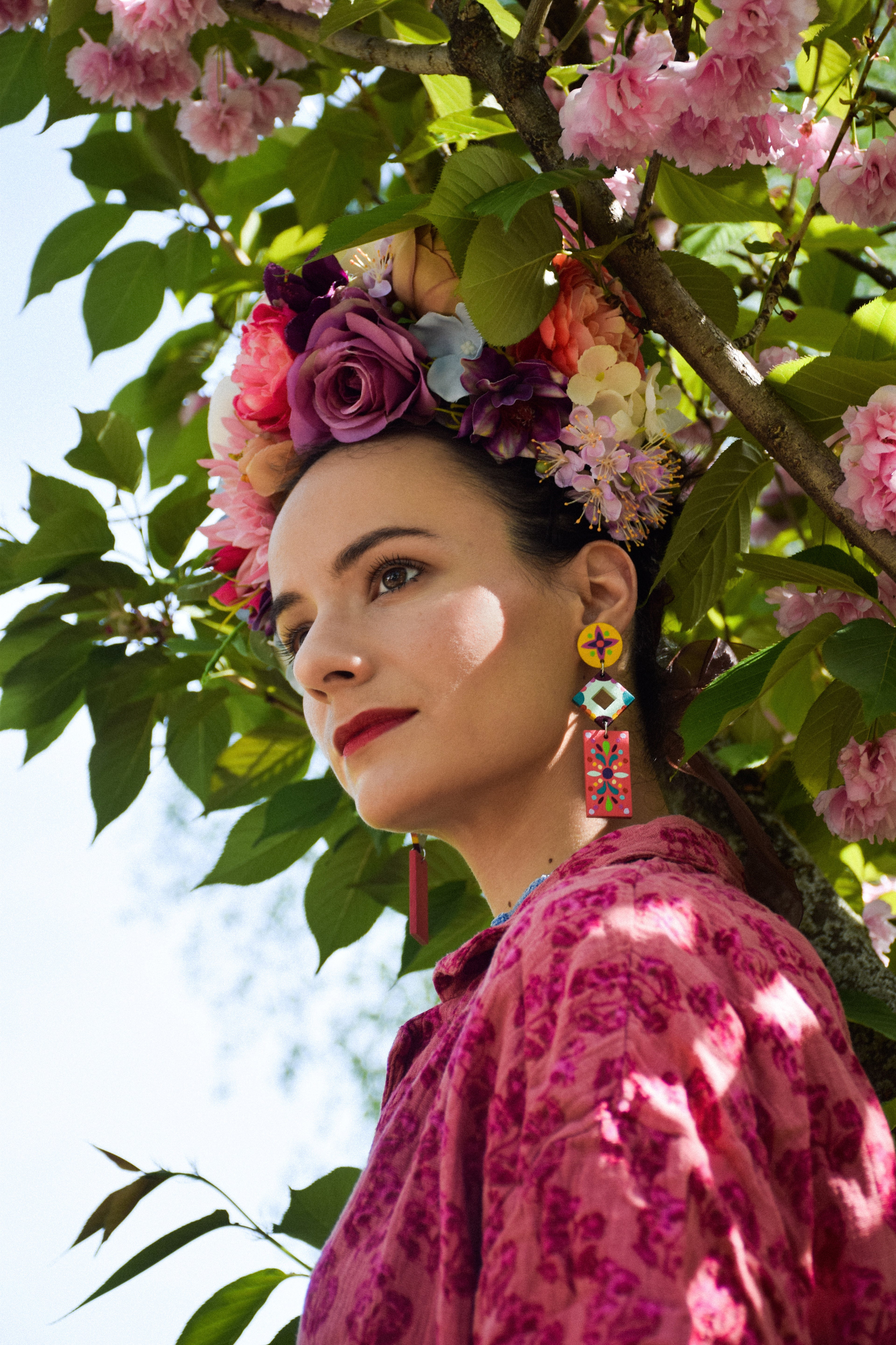 Woman with floral headpiece, colorful earrings and pink dress standing under cherry blossoms