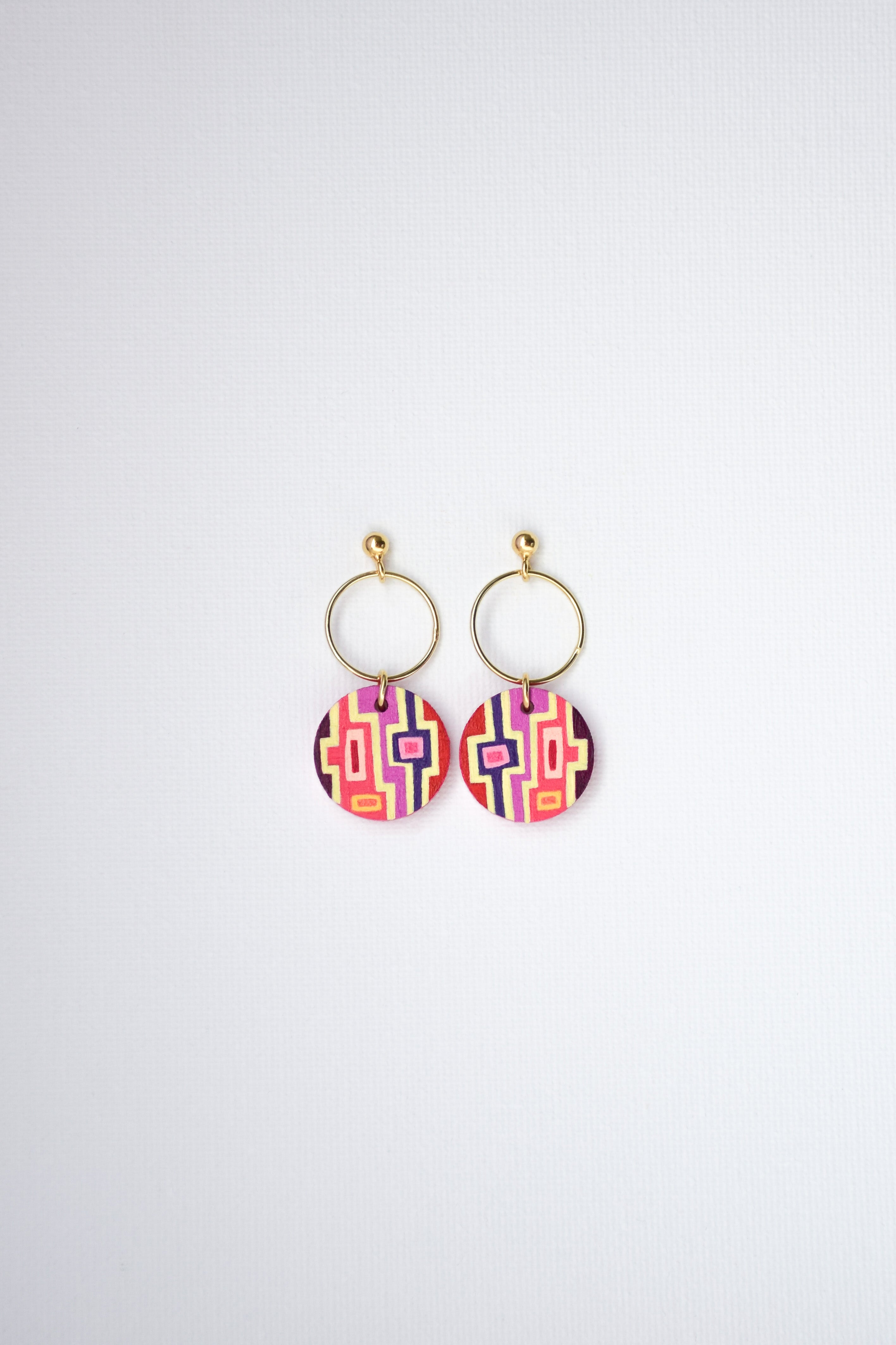 Pair of hand-painted earrings with colorful geometric designs and gold-plated silver hoops on a white background