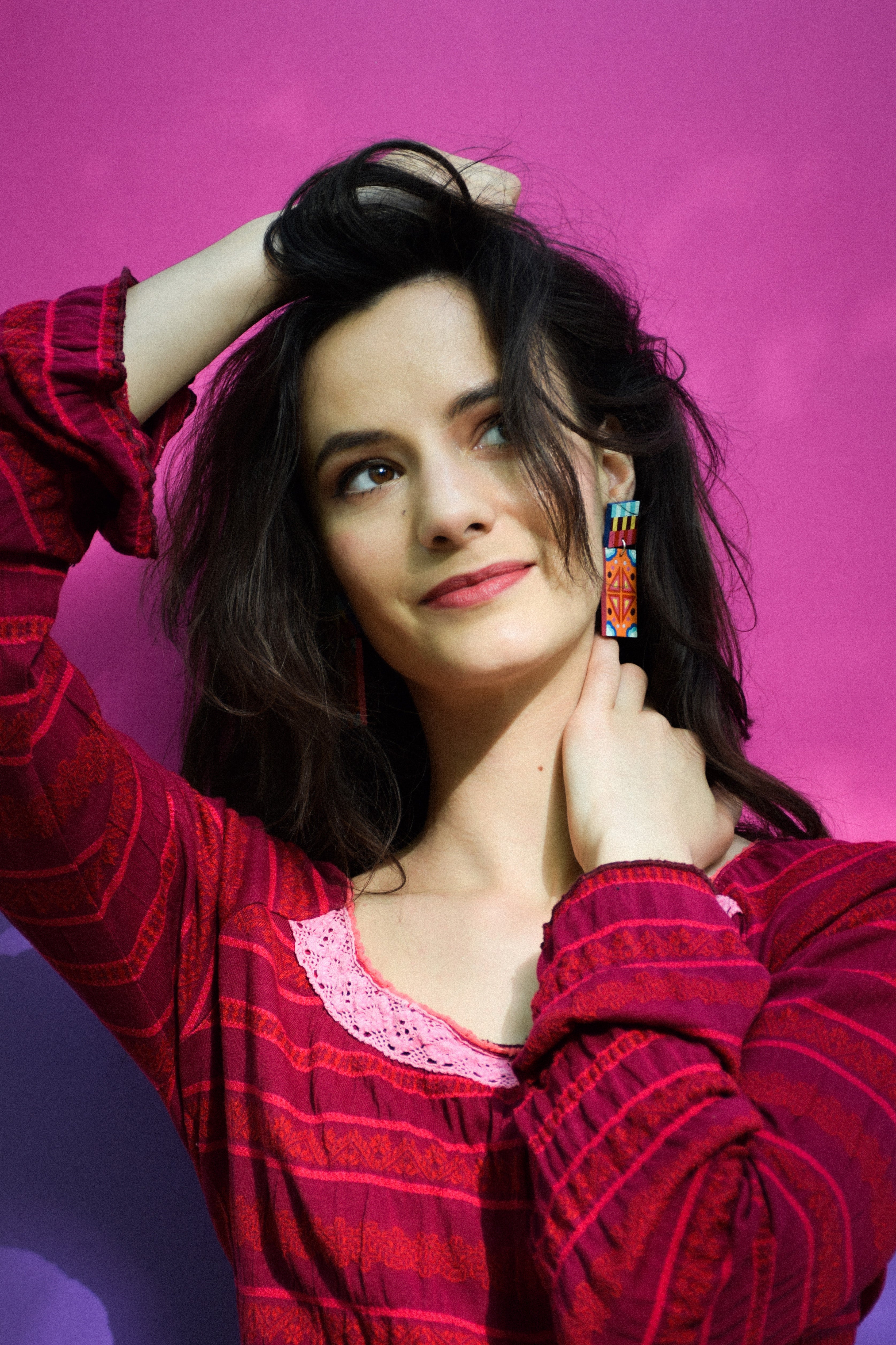 Woman in a red plaid shirt and colorful earrings against a pink background