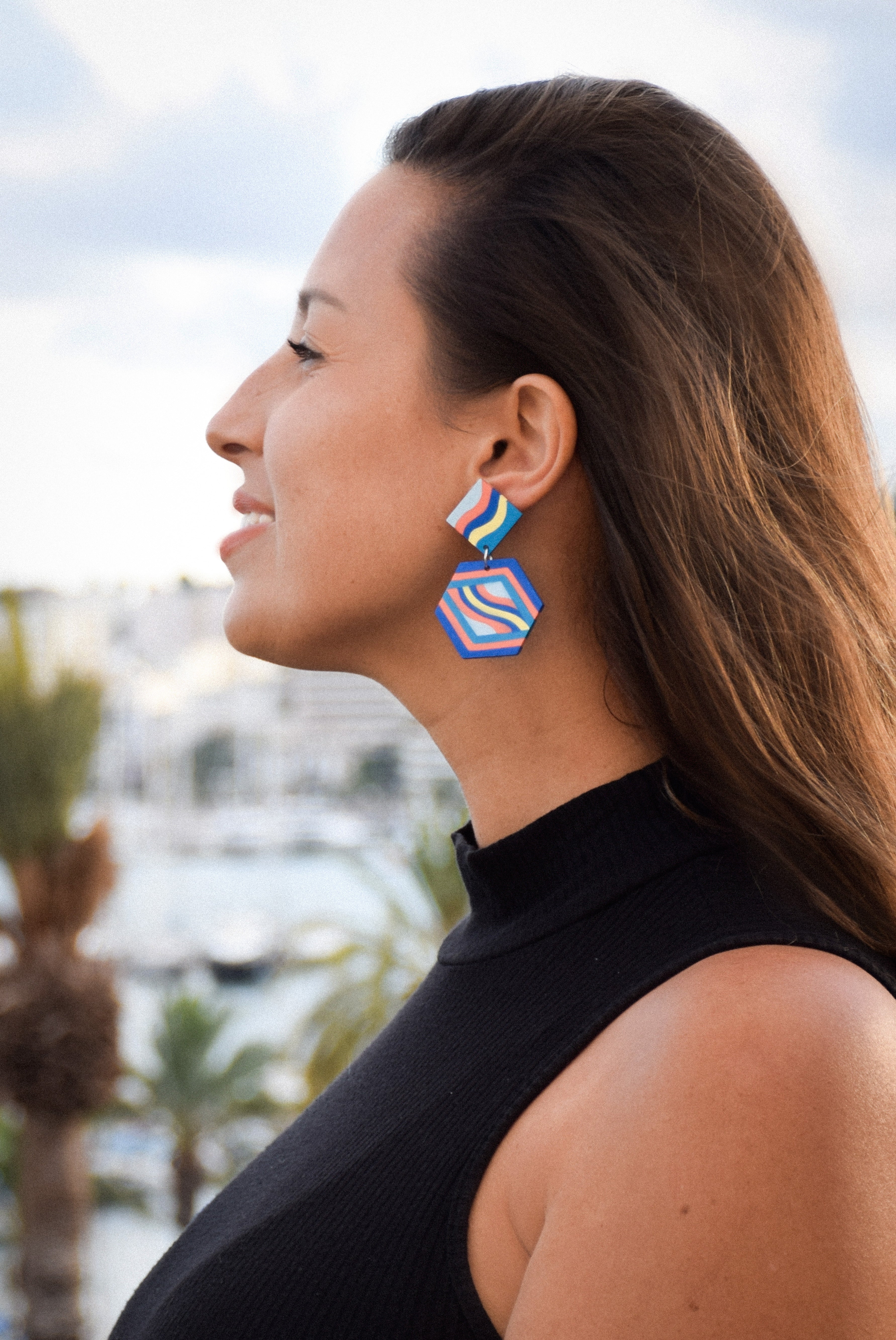 Woman wearing colorful geometric earrings with a blurred outdoor background