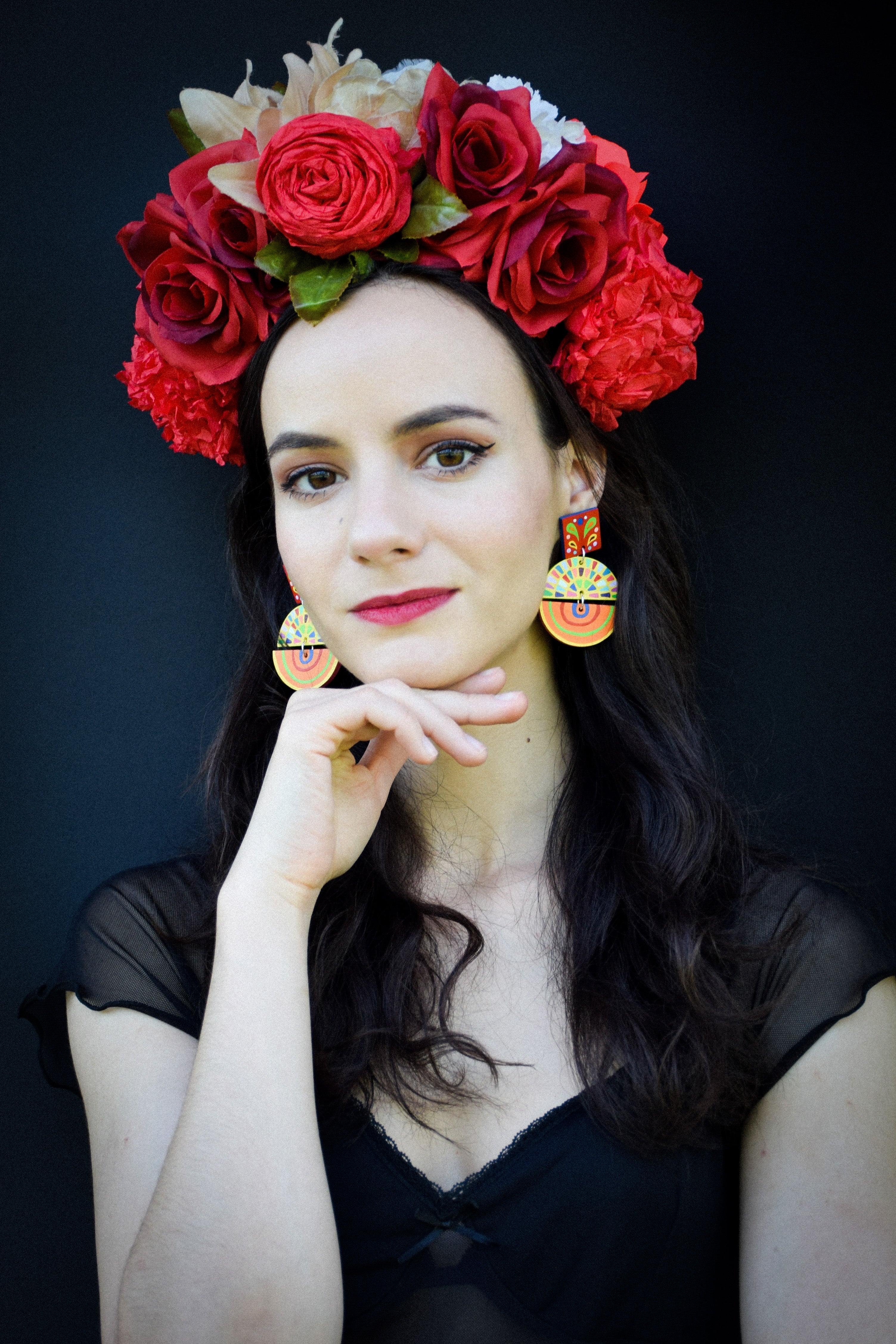 Woman wearing a floral headpiece with red roses and colorful earrings against a dark background