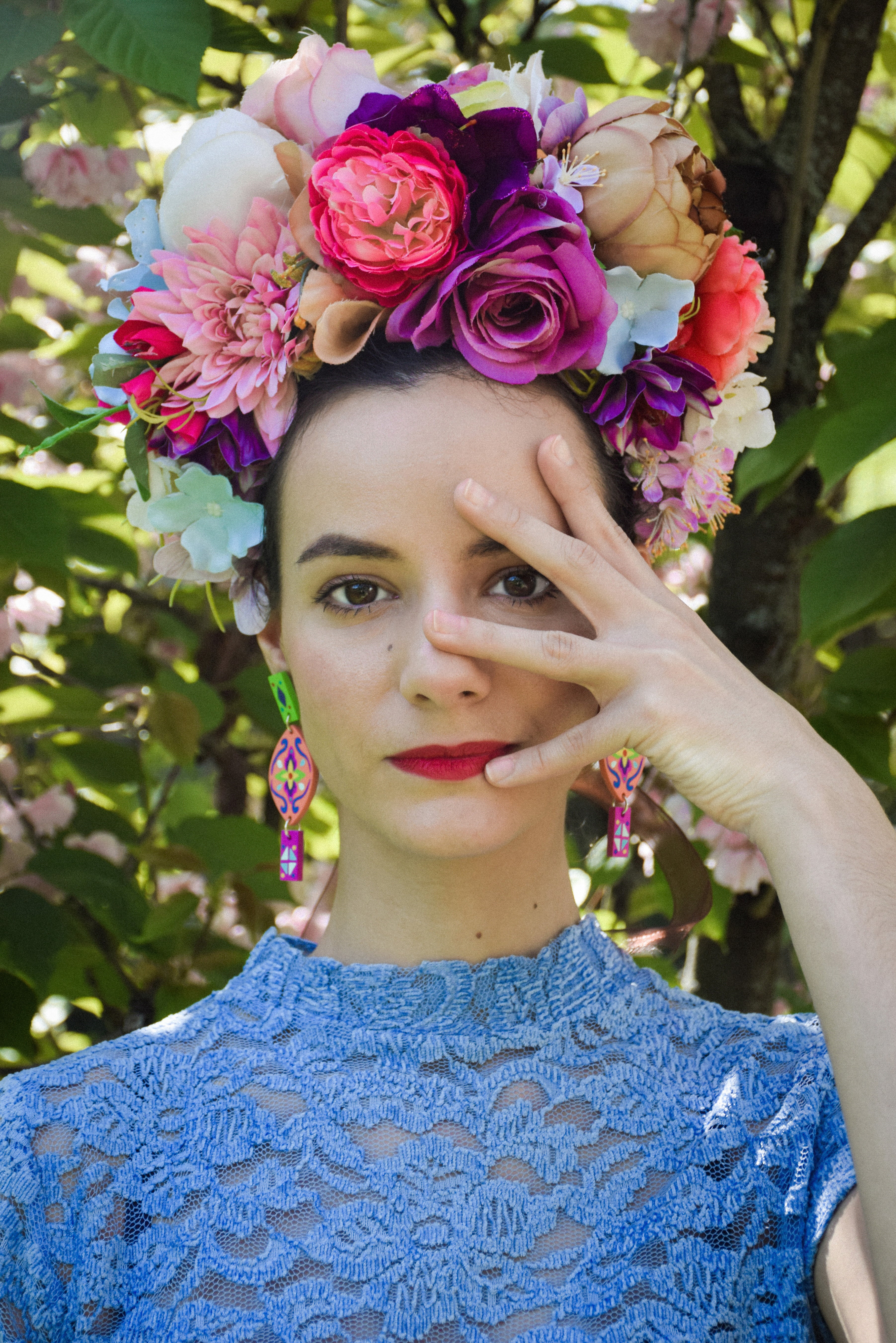Woman wearing a floral headpiece, colorful earrings and blue lace dress with a blurred natural background