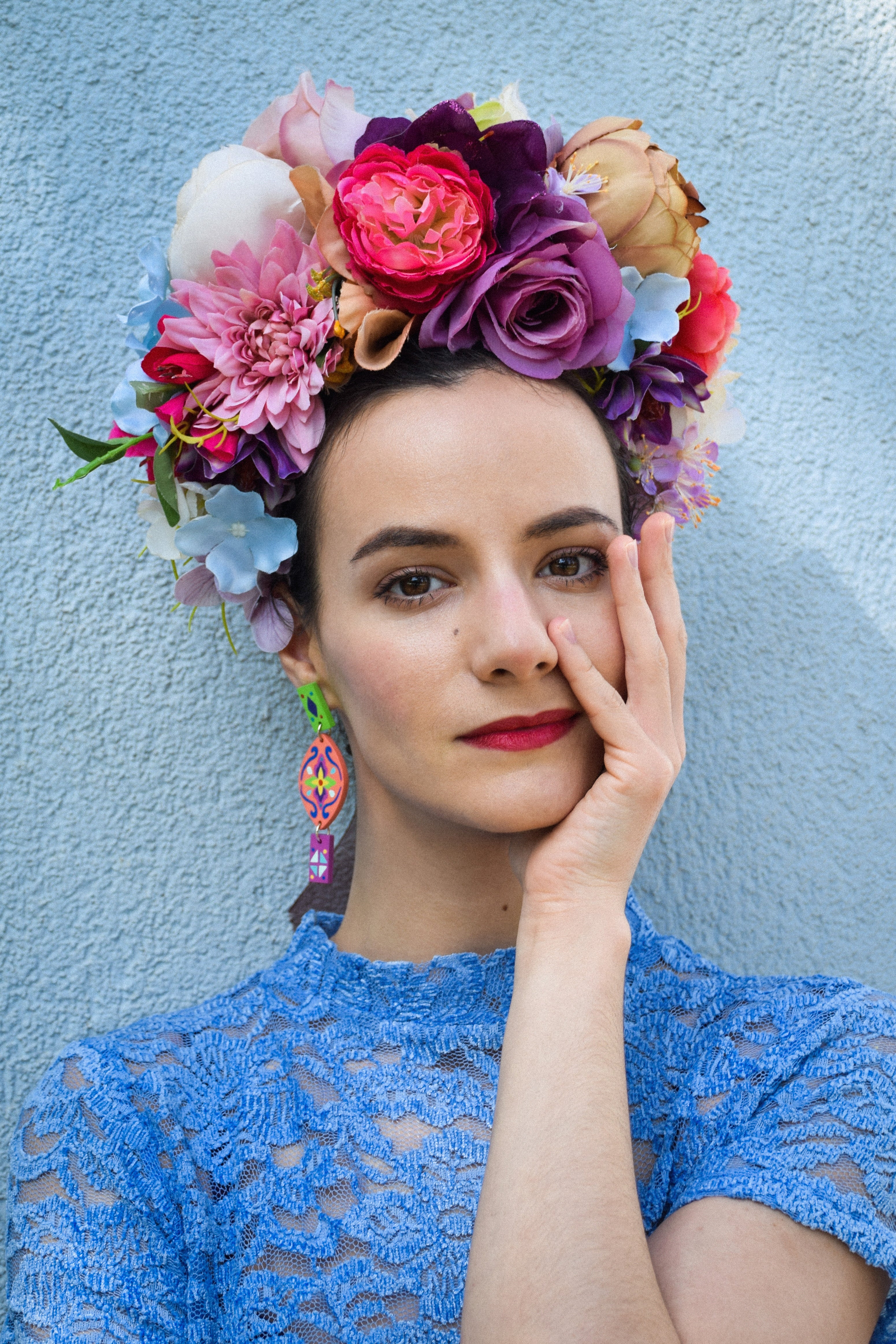 Woman wearing a colorful floral headpiece and colorful earrings against a light blue background